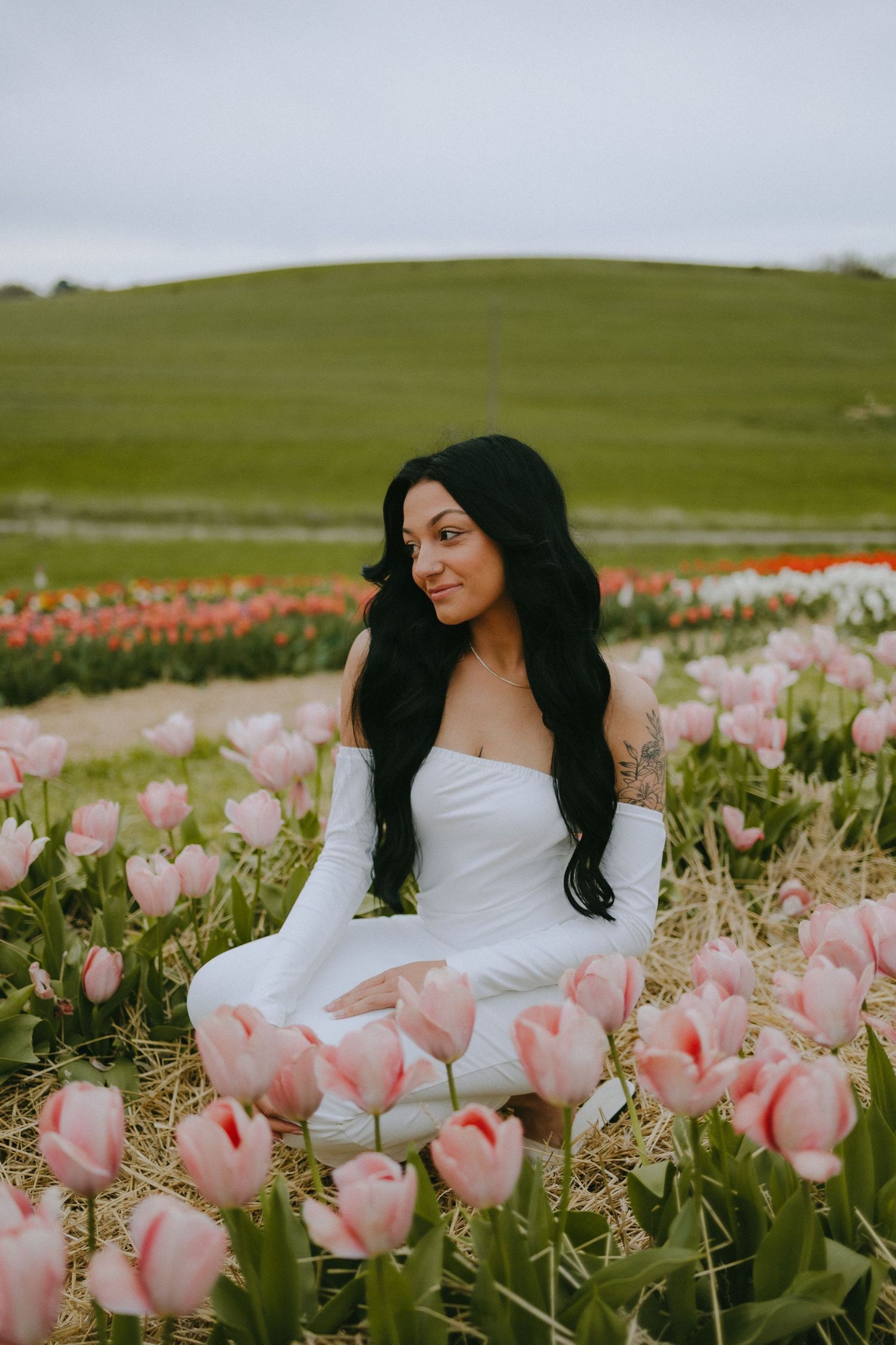 Portrait in white dress amidst blooming pink tulips on rolling hills.