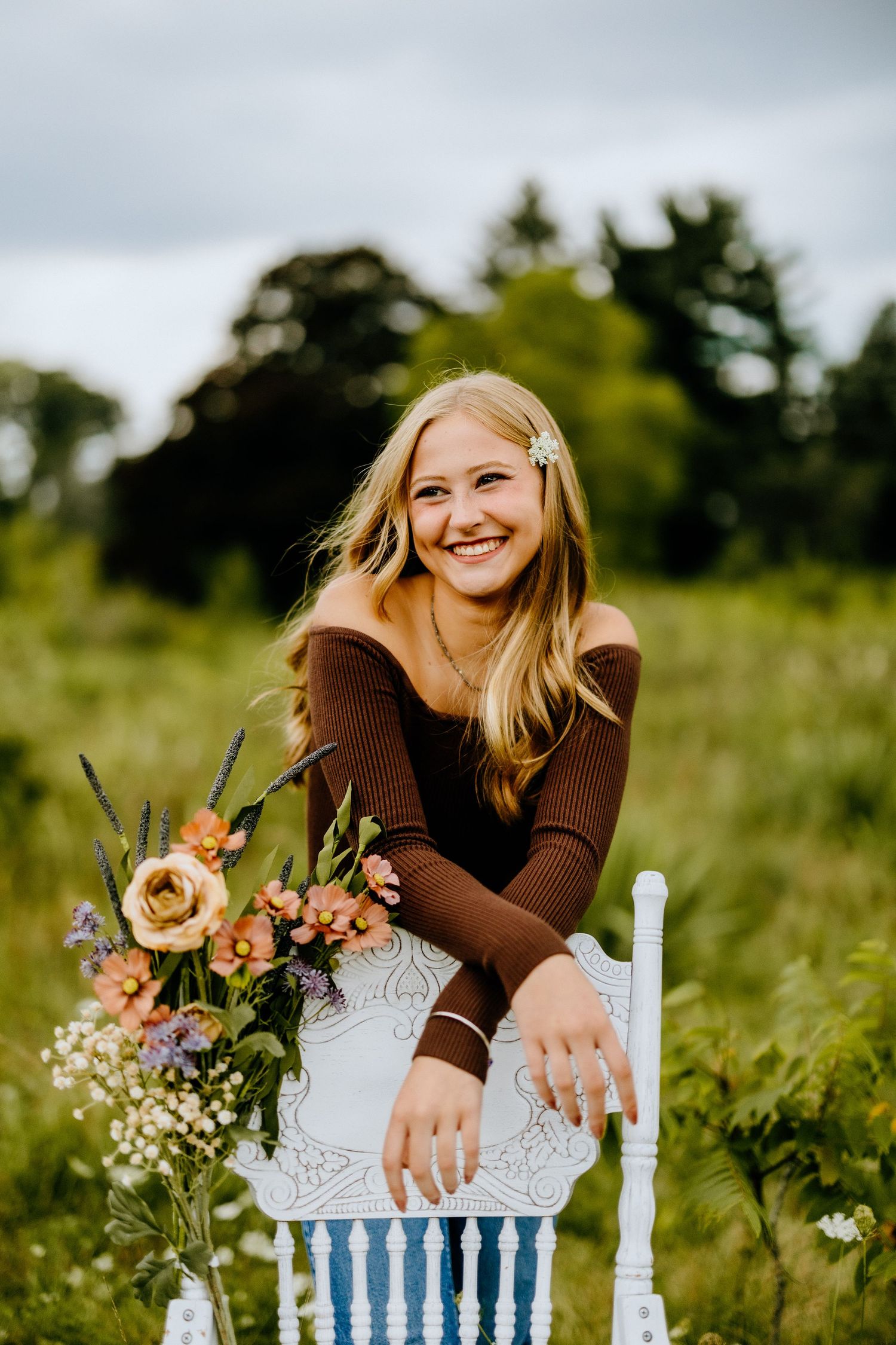 Person in brown sweater sits on vintage chair with peach floral arrangement in meadow.
