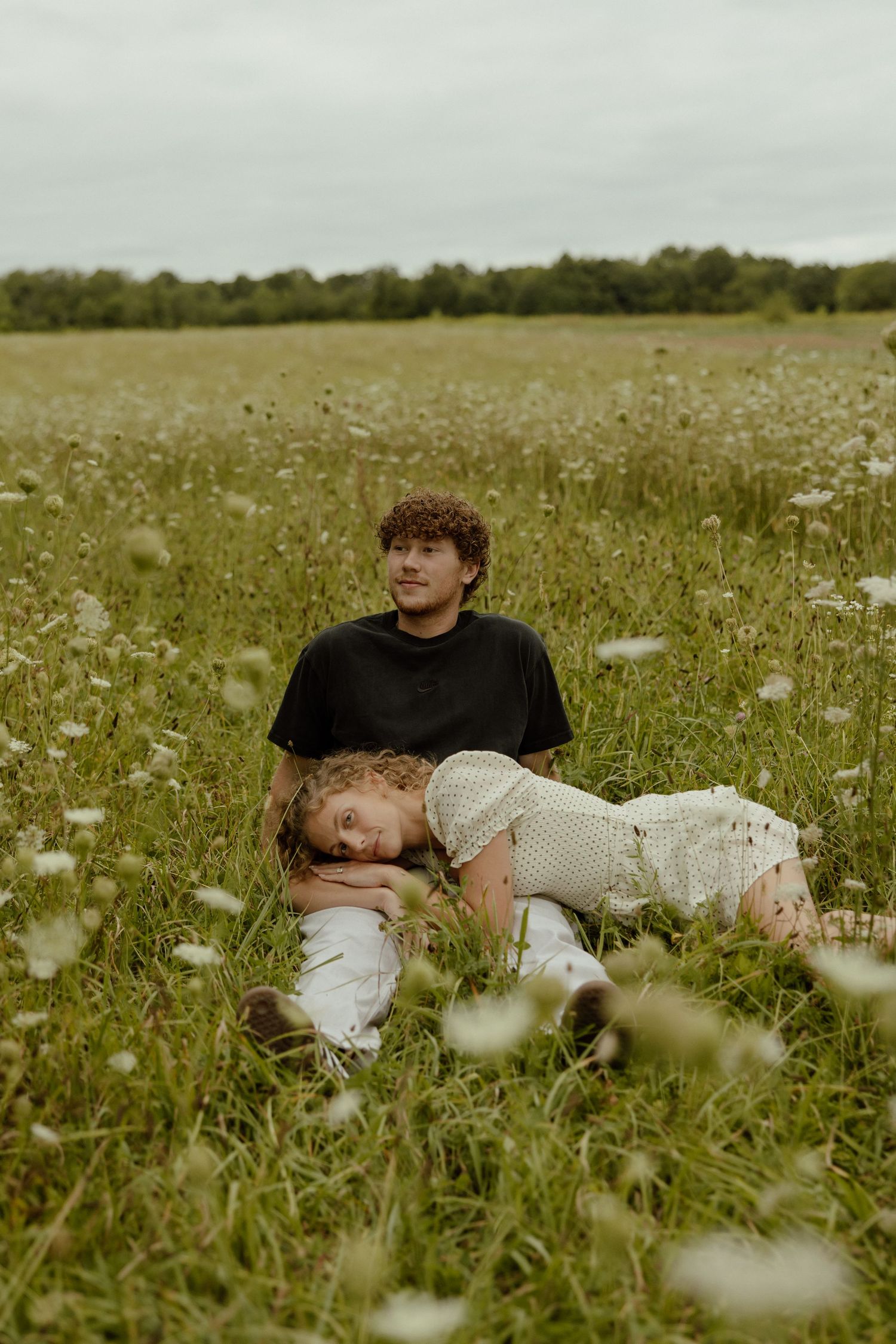 Two people relax together in a serene wildflower meadow on an overcast day.