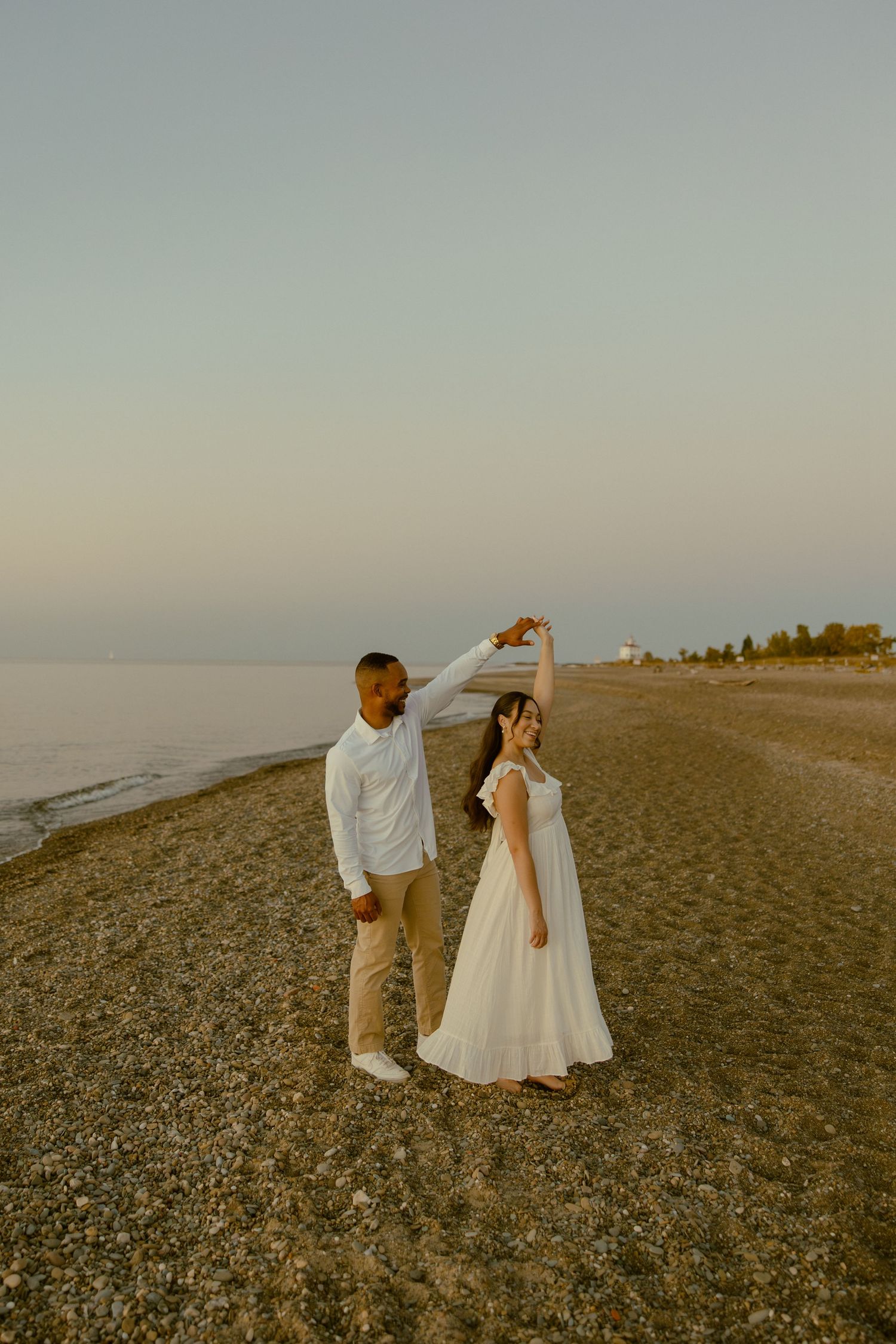 A couple walks together on a rocky beach at sunset, creating a romantic silhouette against the golden sky.