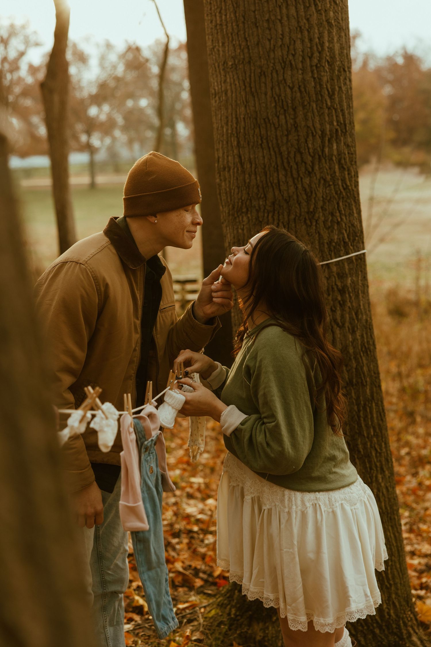 A romantic autumn couple in casual attire share intimate moments among fallen leaves and trees.