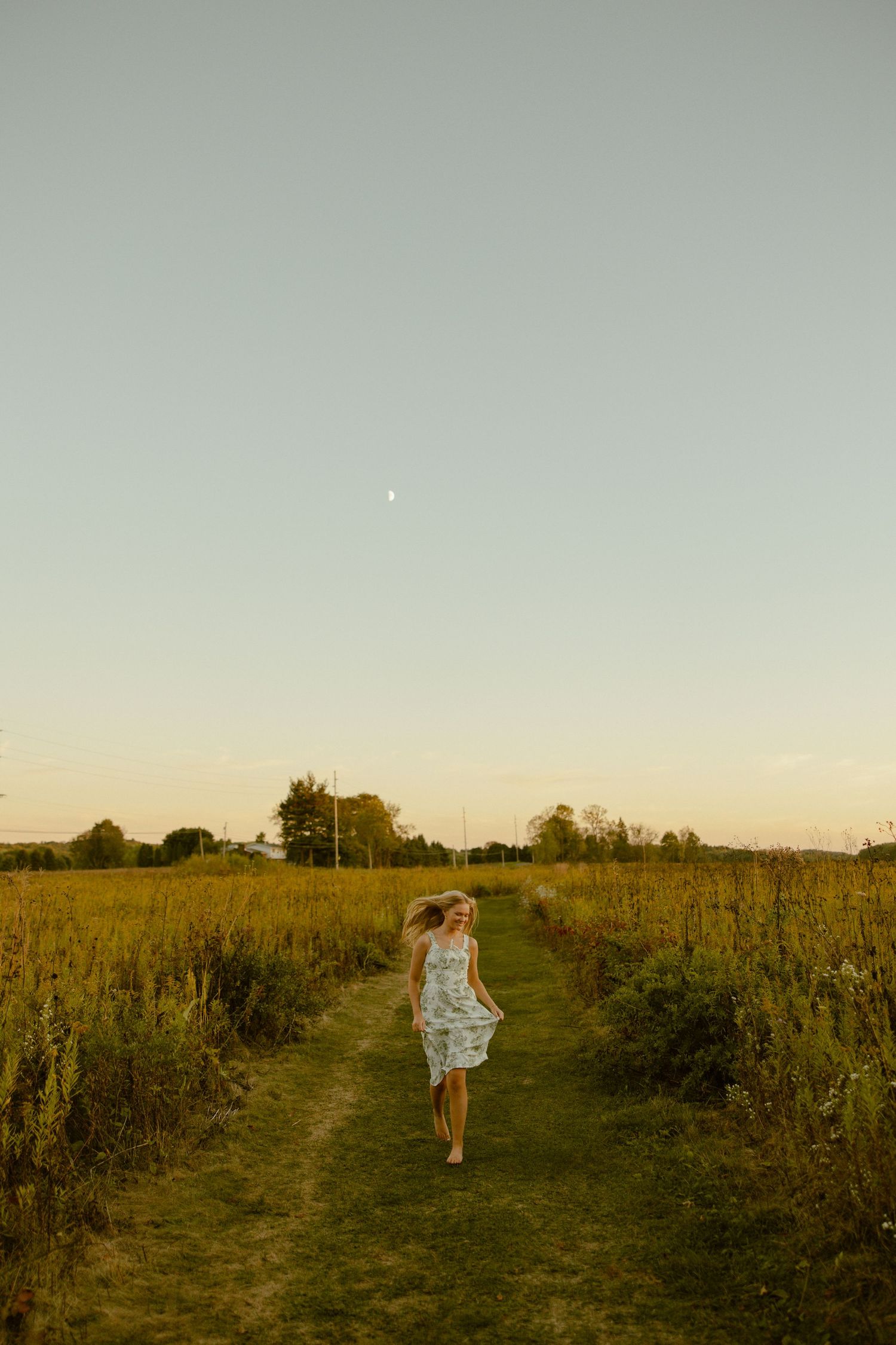 A dirt path winds through a golden summer meadow at sunset with wildflowers and tall grasses on either side.