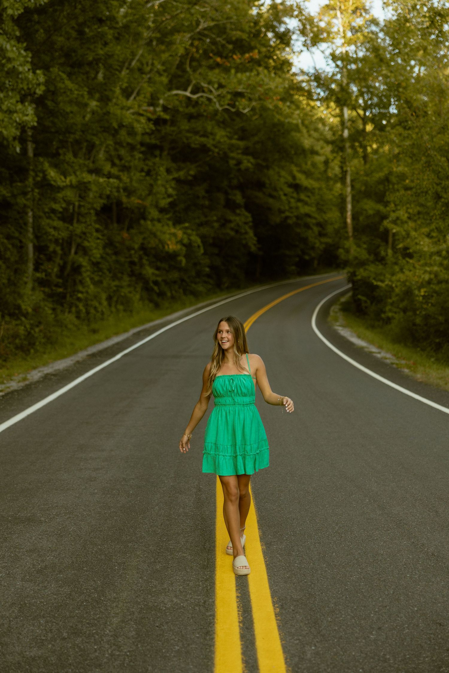 A sequence of shots showing a person in a bright green top standing on a curved forest road with yellow lines.