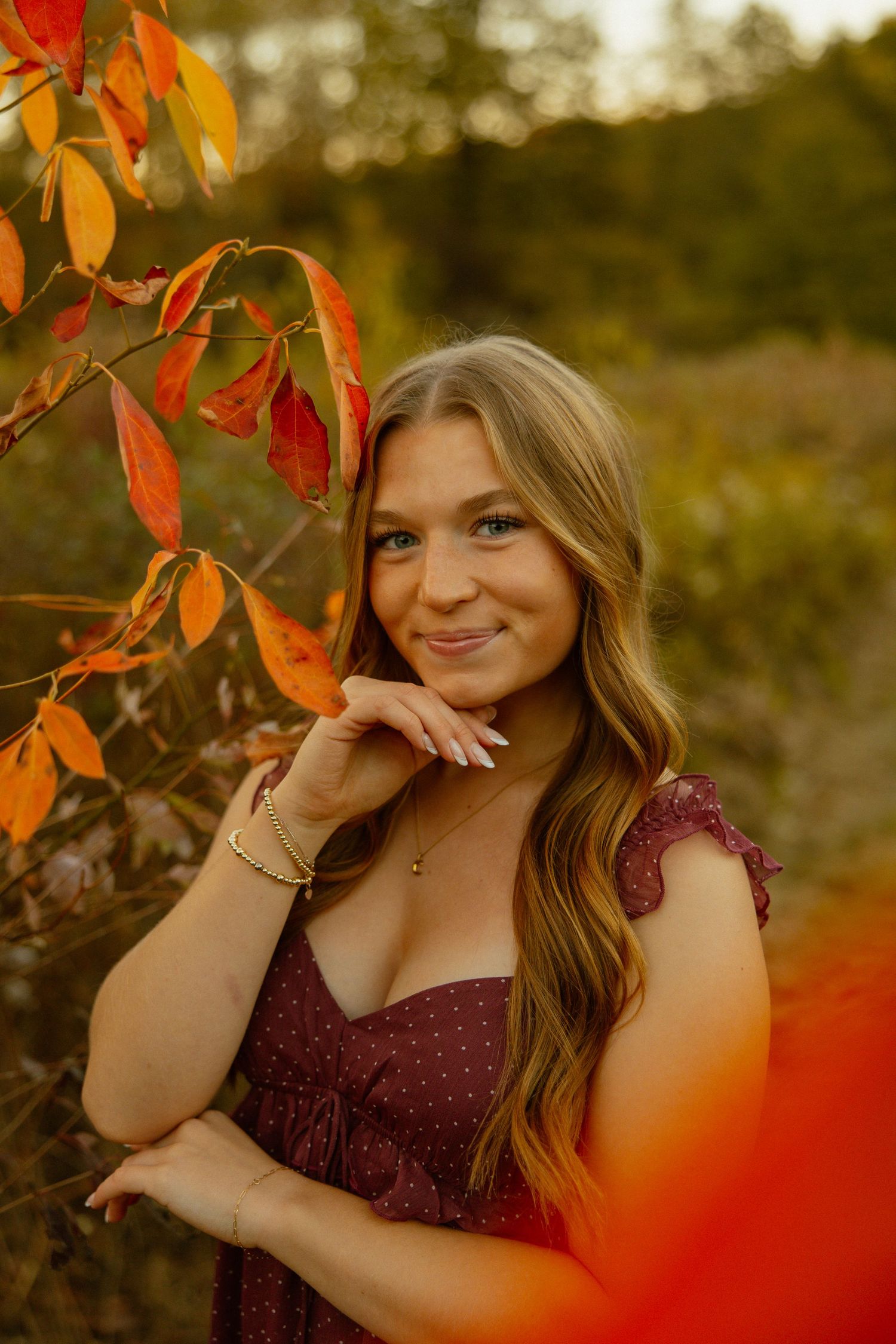 Autumn portrait session featuring warm orange foliage and a burgundy dress in golden hour lighting.