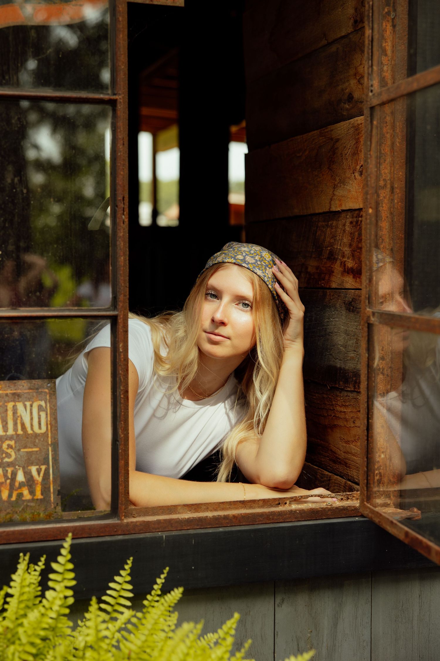 A vintage wooden window frame with ferns growing below creates a rustic portrait setting.