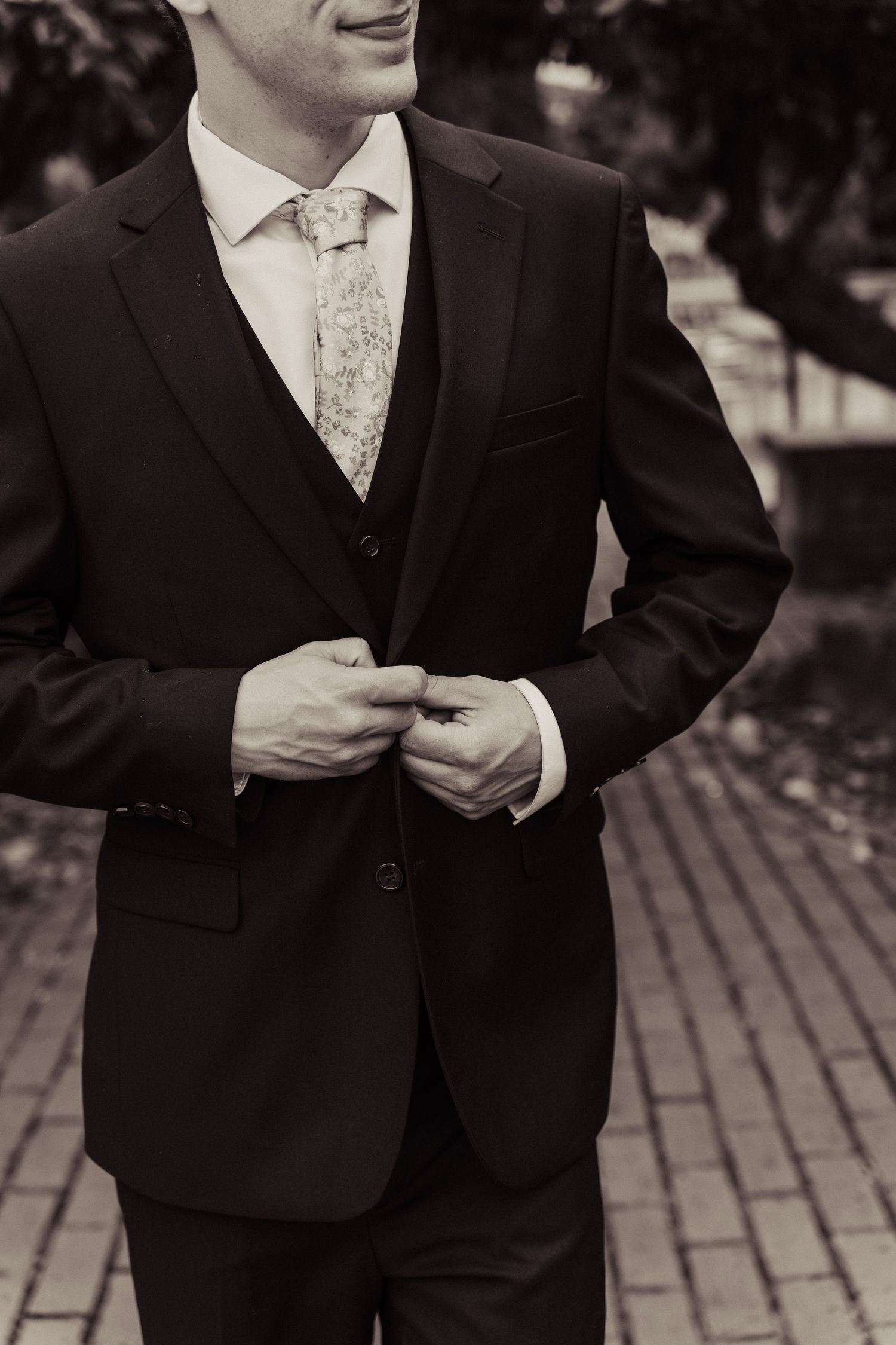 Close-up view of groomsmen in black suits adjusting their jackets and ties in a formal wedding setting.