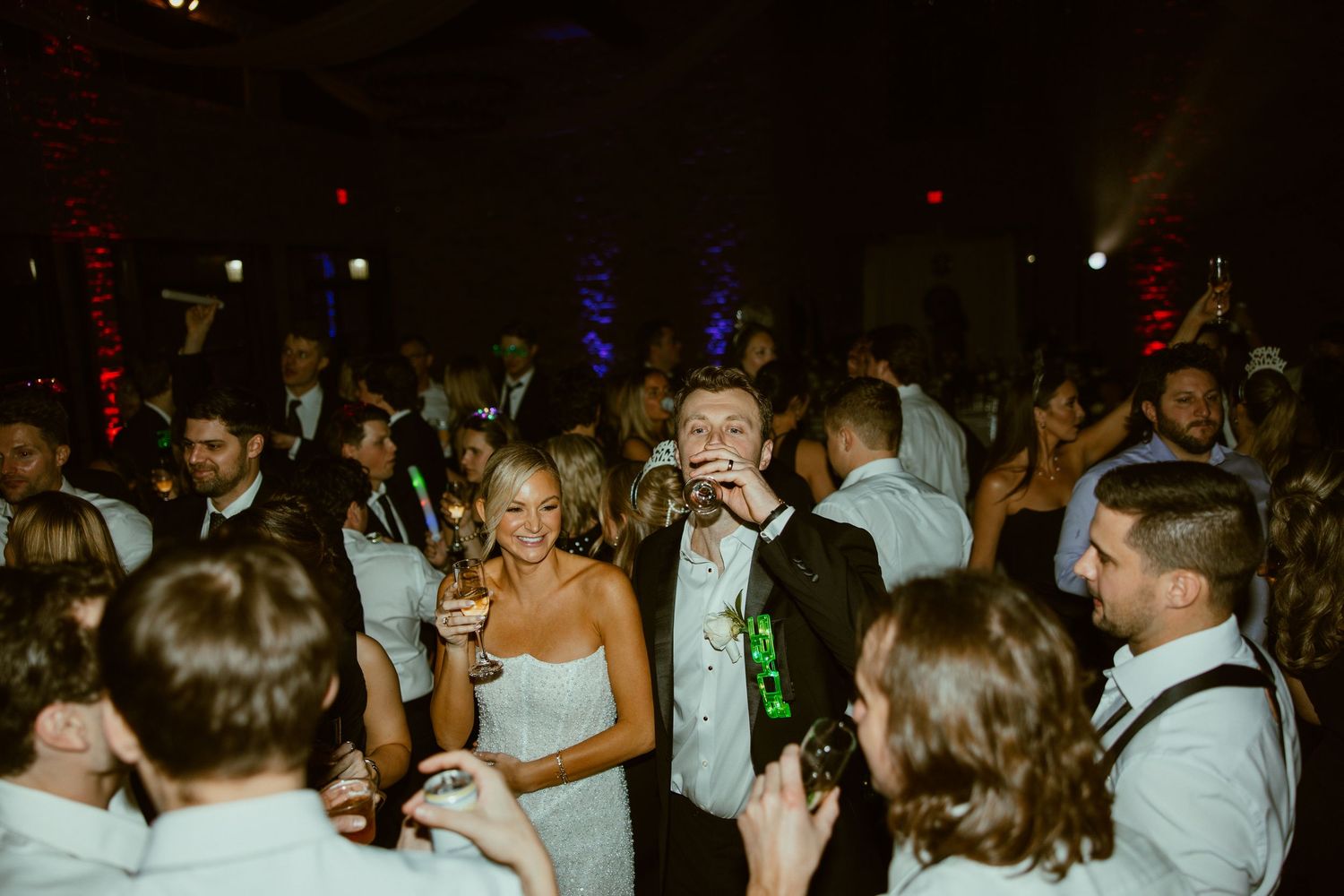 Wedding reception dance floor filled with guests celebrating under dim lighting.