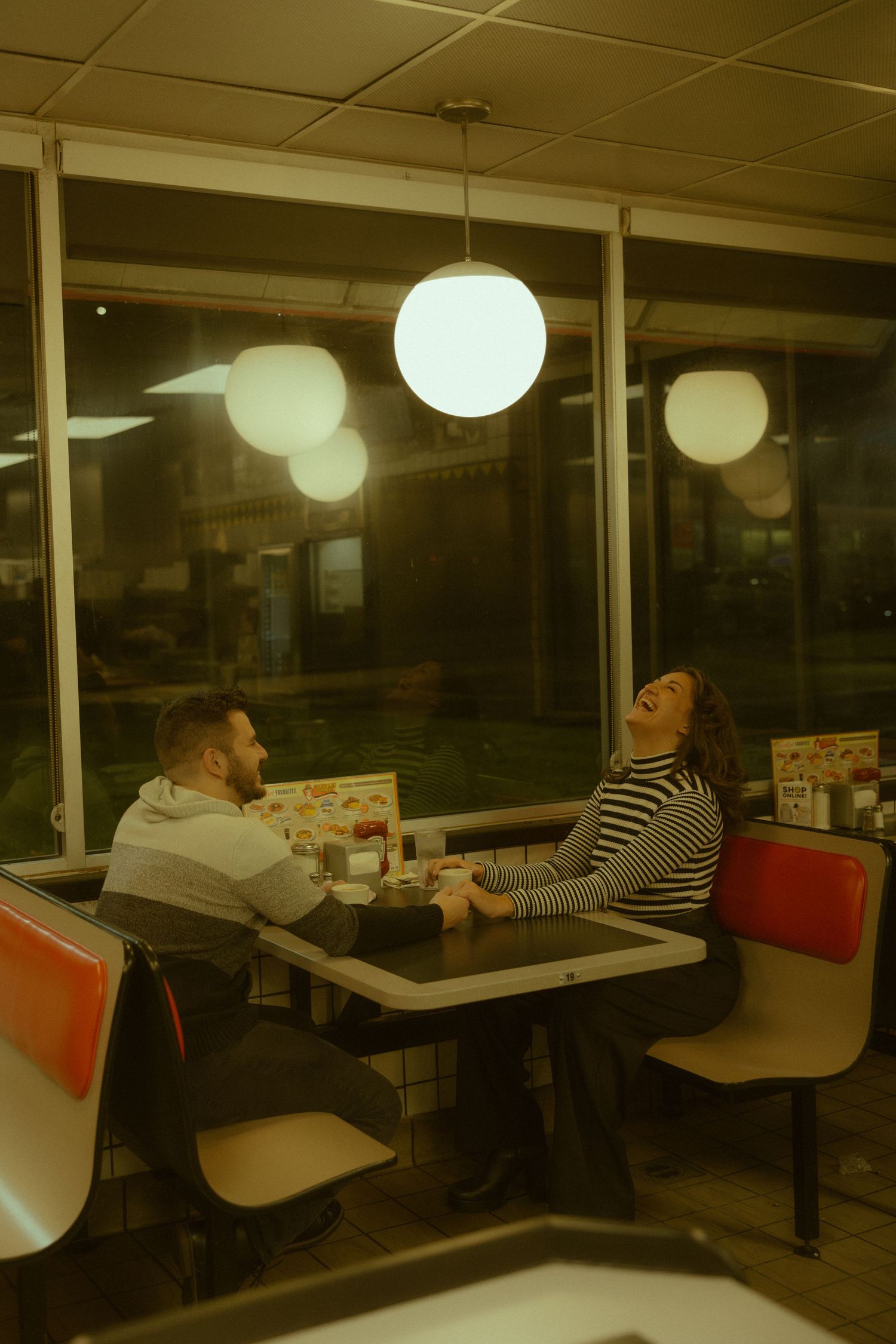 Customers seated in booths at a dimly lit restaurant with round pendant lights creating a cozy evening atmosphere.