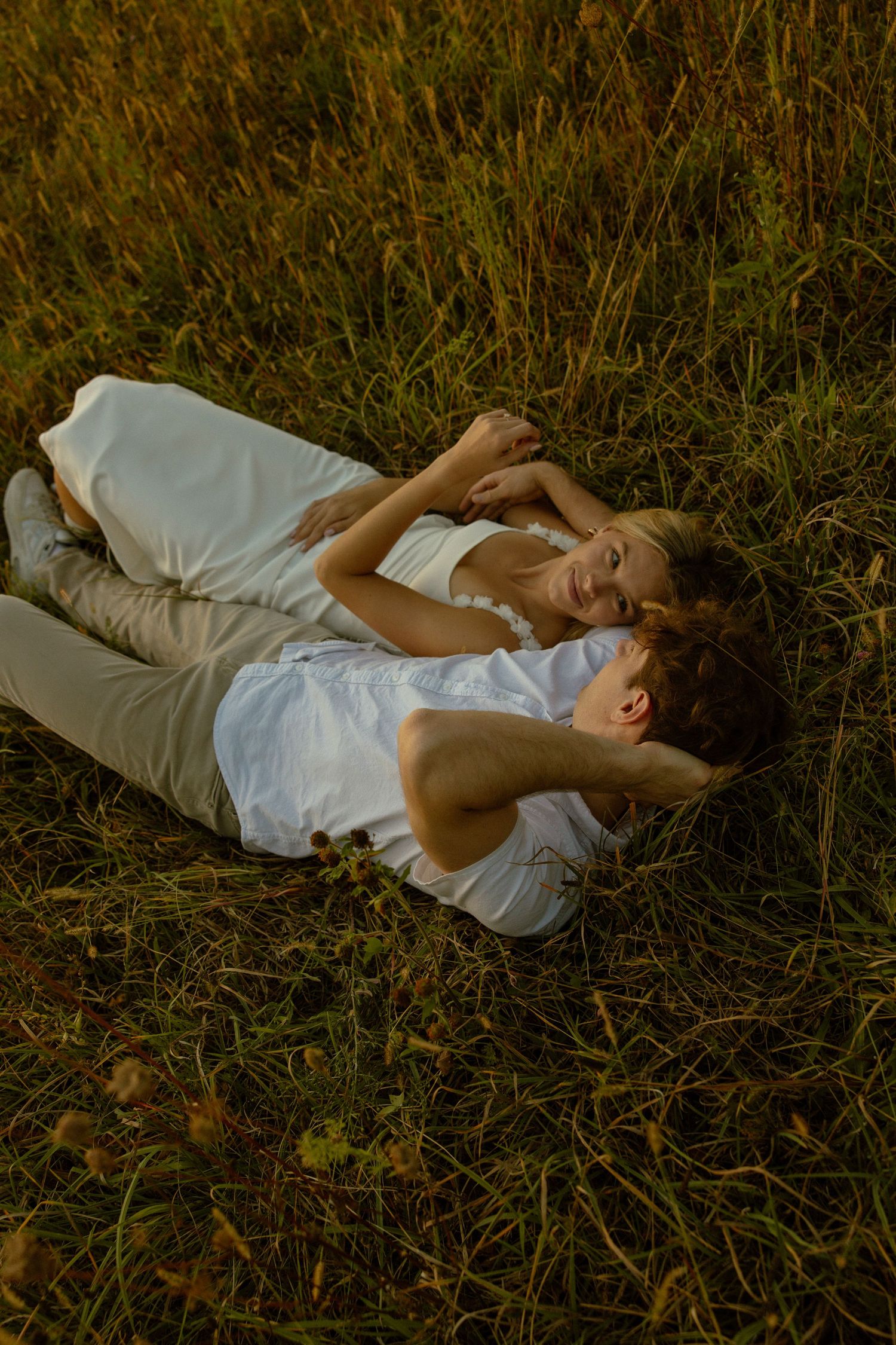 A person in a white dress lies peacefully in tall grass during golden hour, creating a dreamy outdoor portrait series.