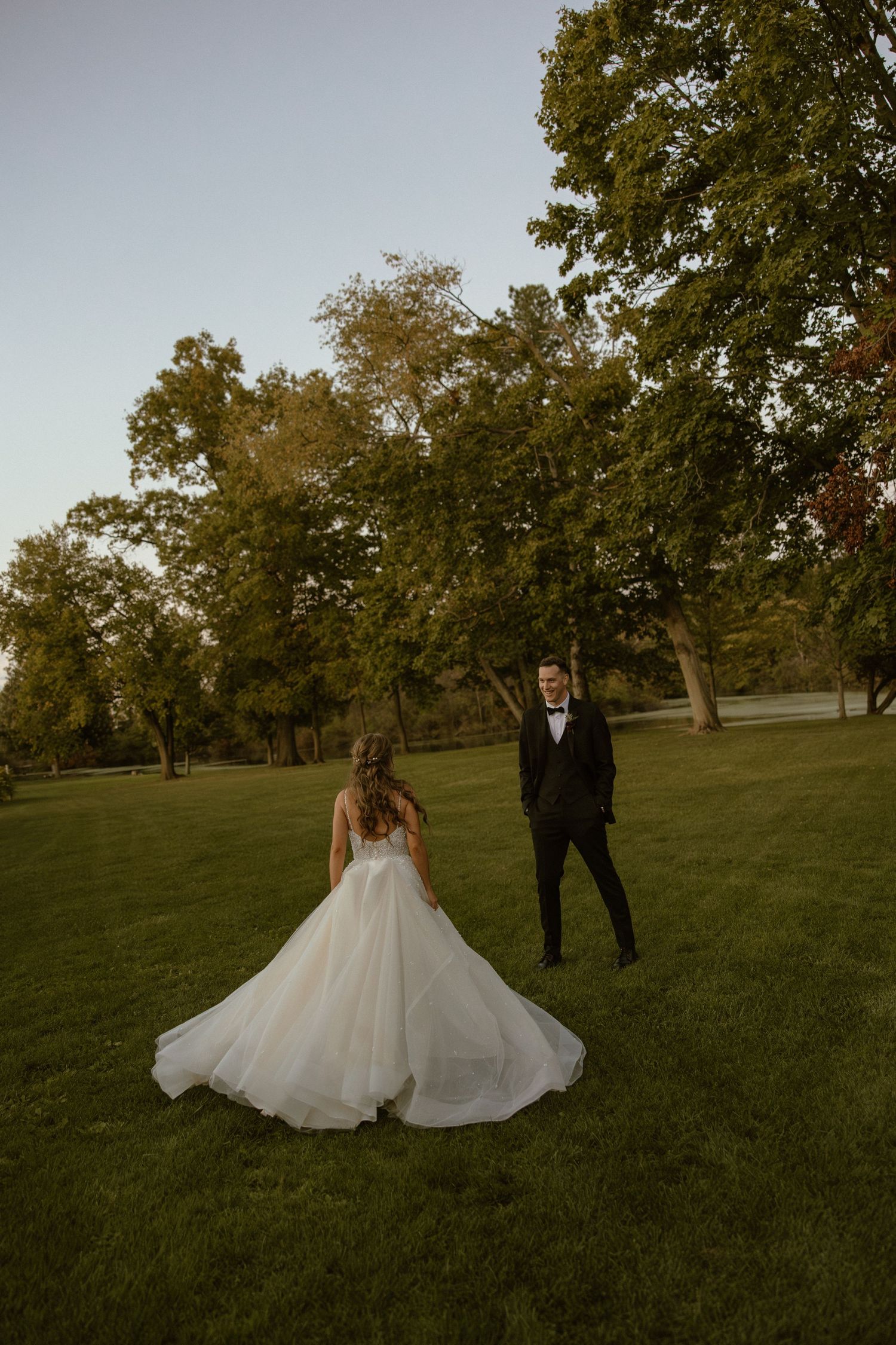 A wedding couple poses in a scenic park setting during golden hour with autumn trees in the background.
