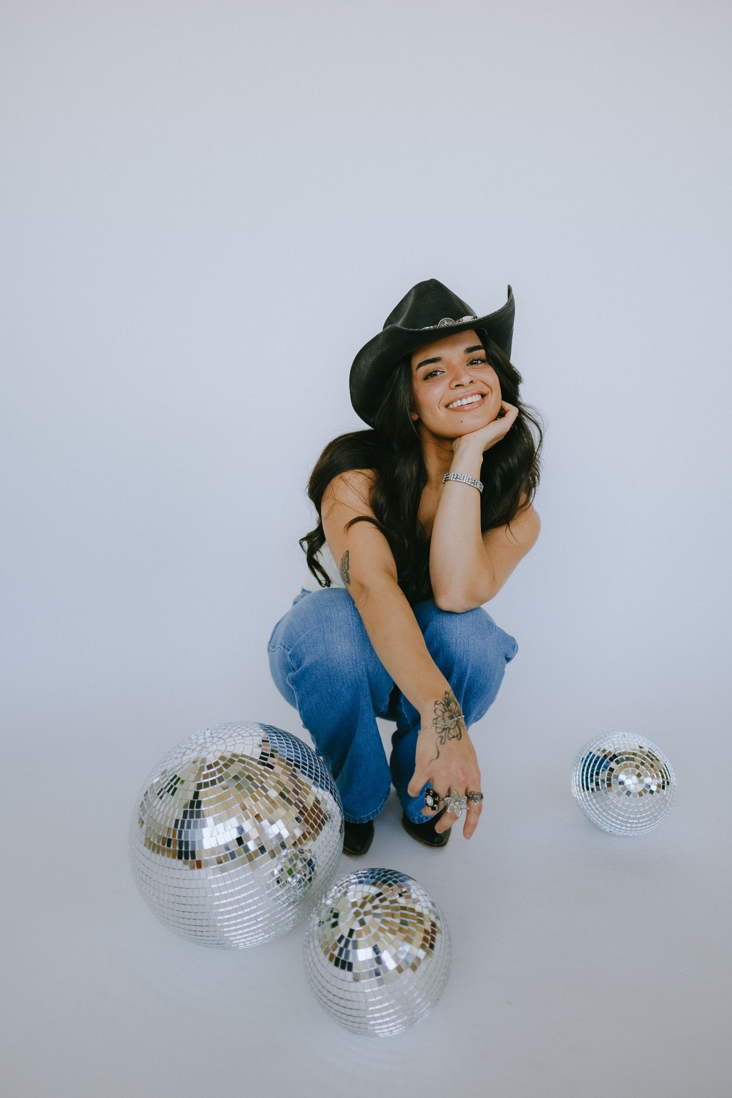 Stylish pose with disco balls and cowboy-inspired outfit on grey background.