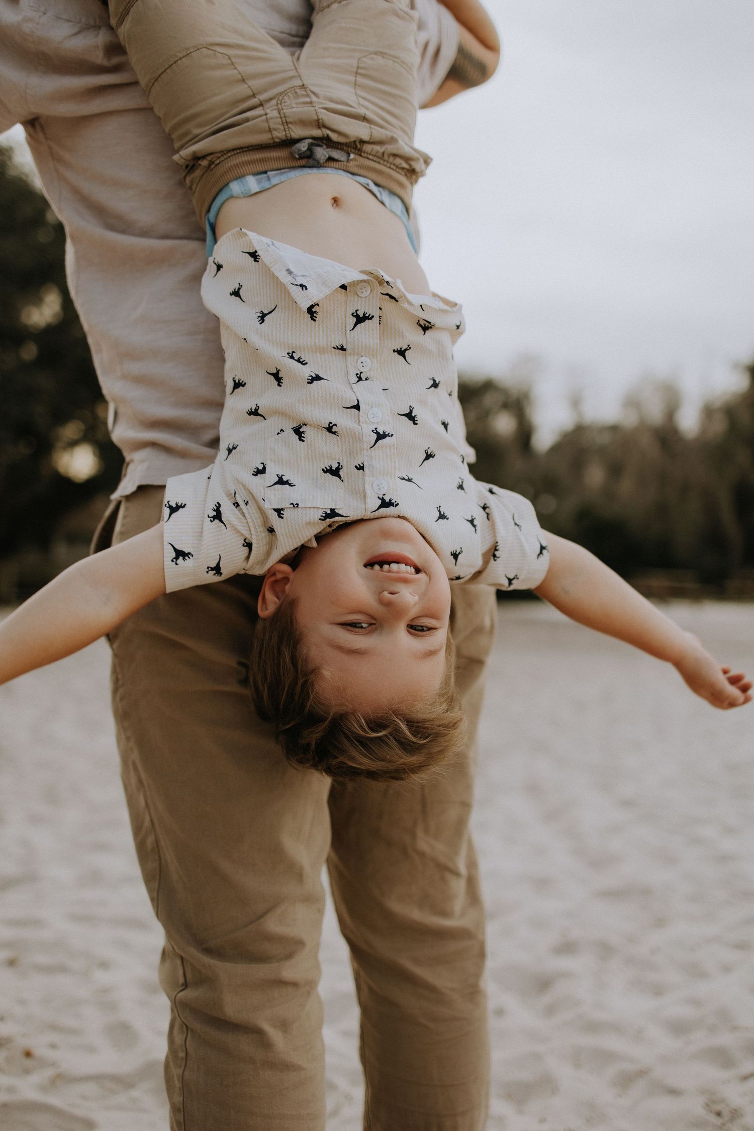 A playful moment captured as a child hangs upside down on a beach.