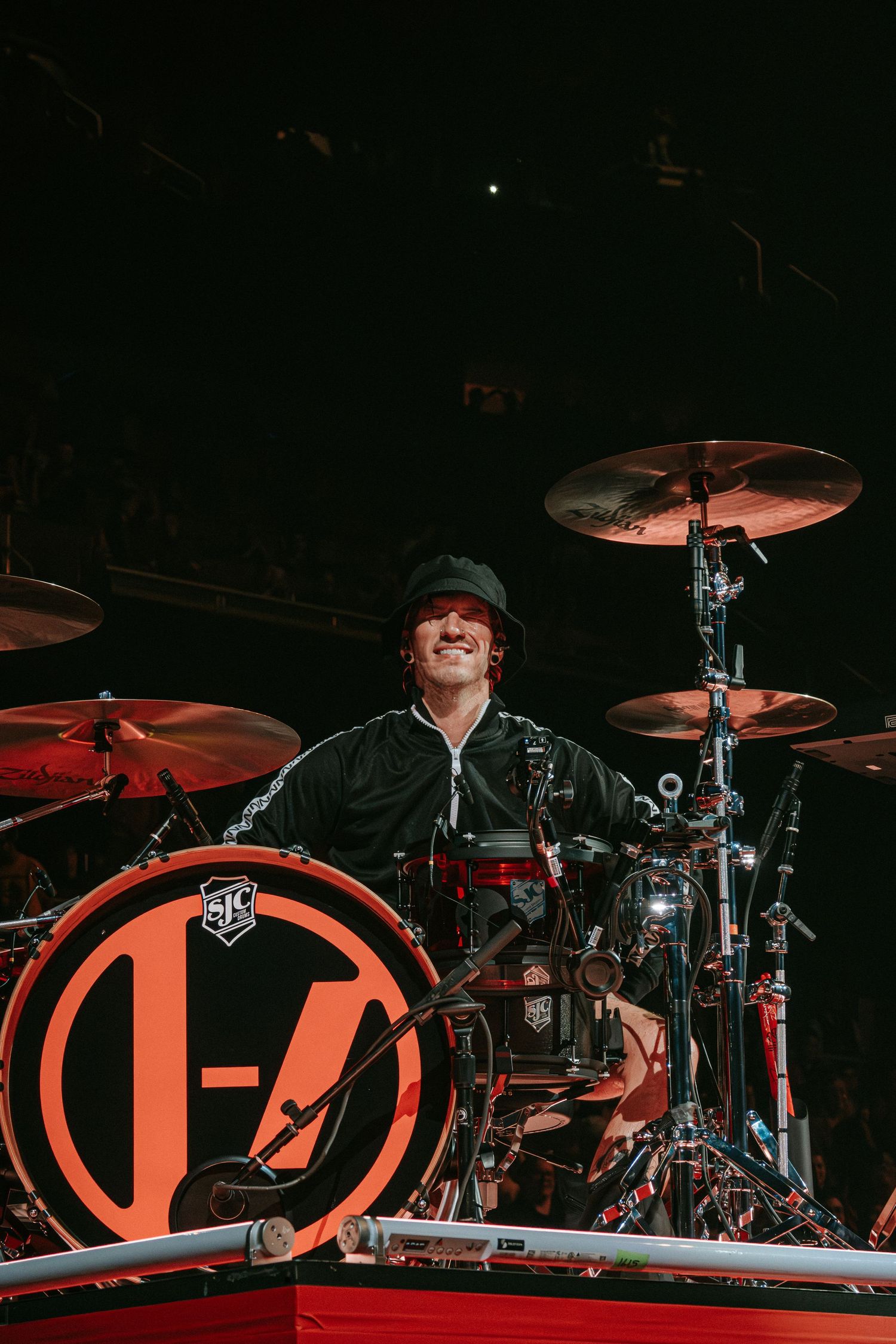 Drummer performs behind large branded drum kit with enthusiastic expression.