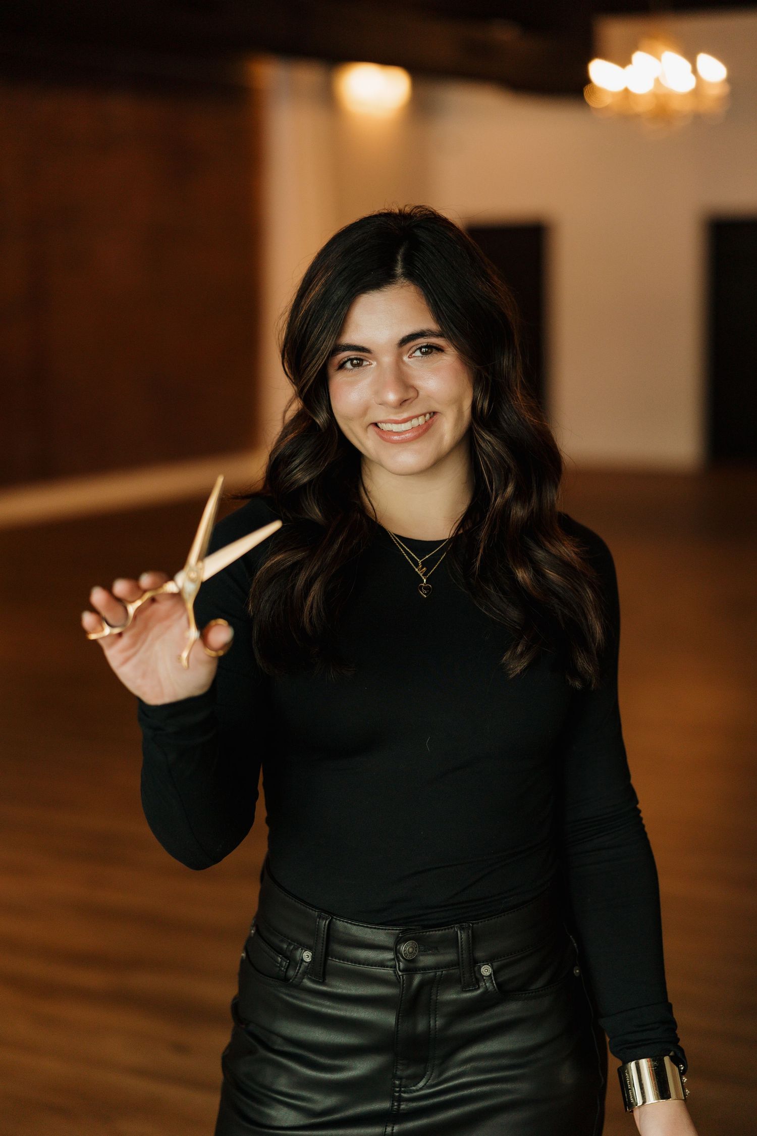 Stylish indoor portrait holding drumsticks while wearing a black top and leather pants.