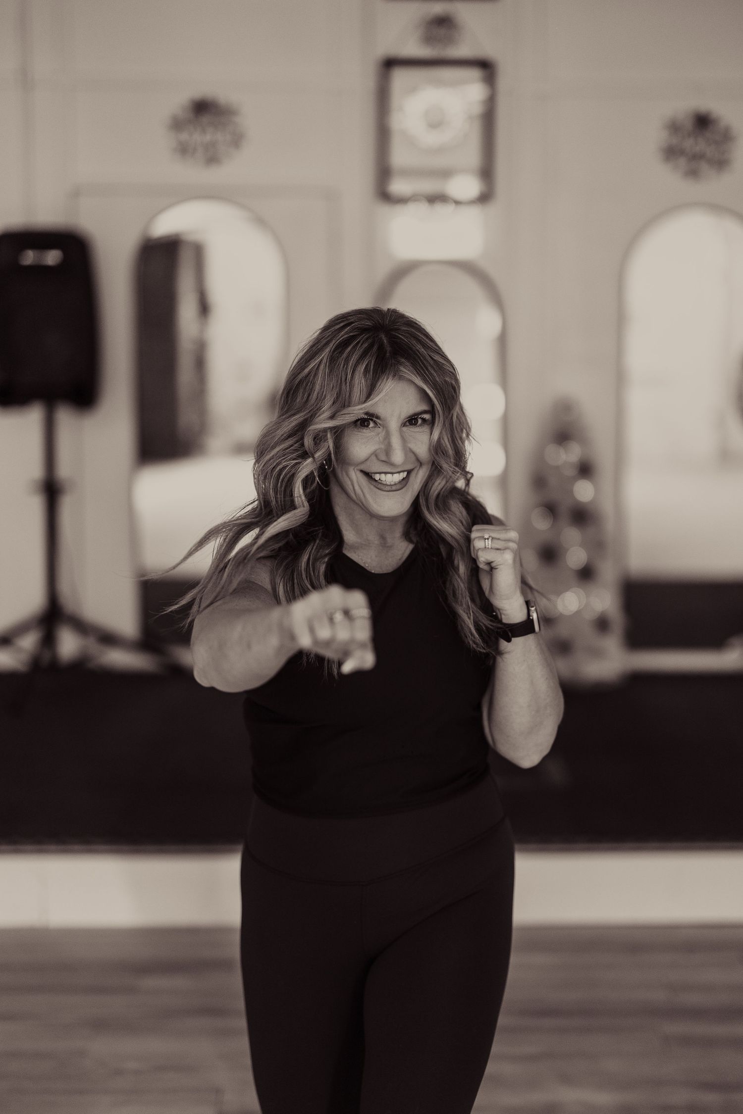 Woman in all-black activewear throws energetic boxing punches in a dance studio setting.