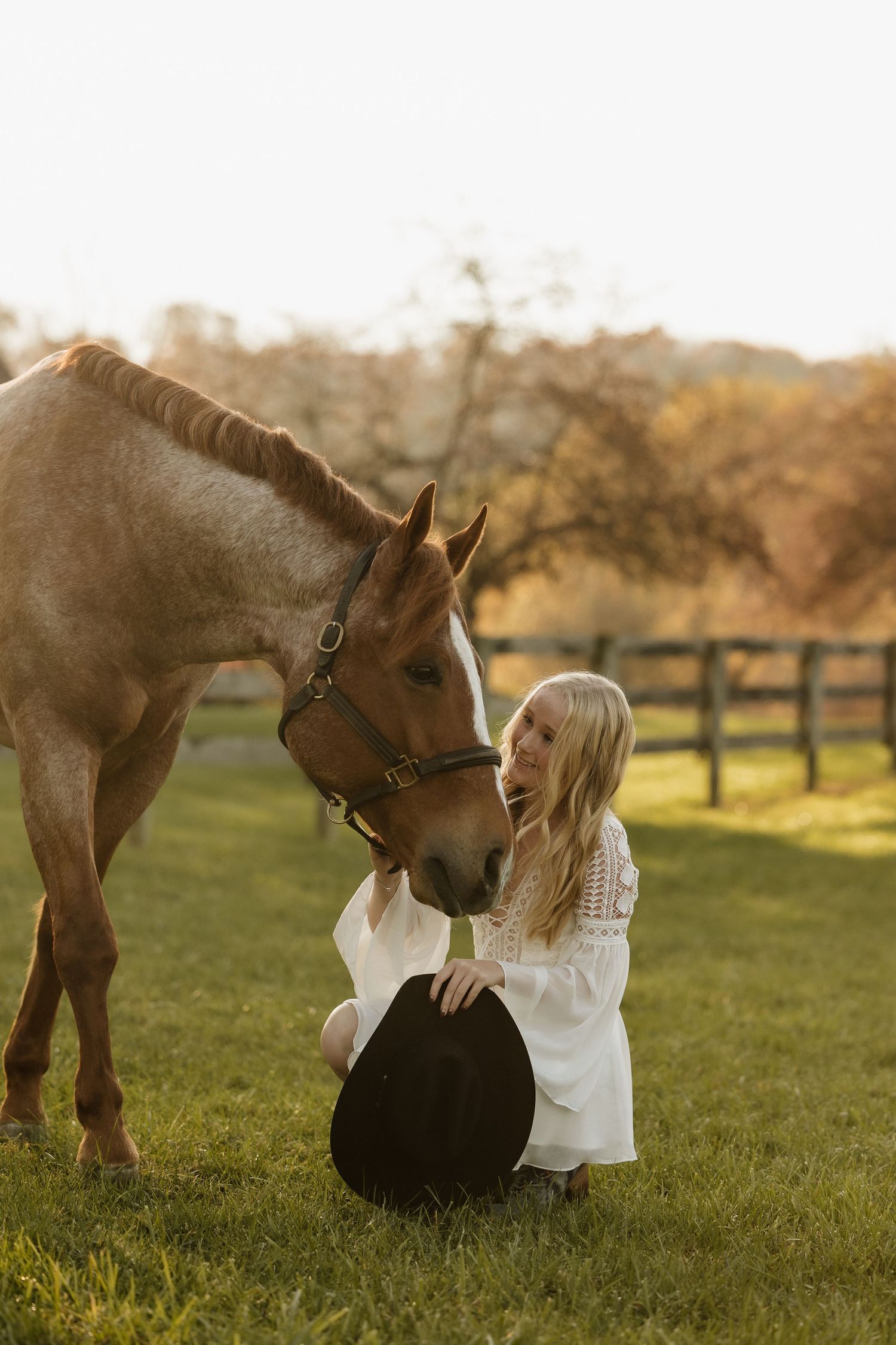 A gentle moment between a person and their horse in an autumn field with wooden fences.