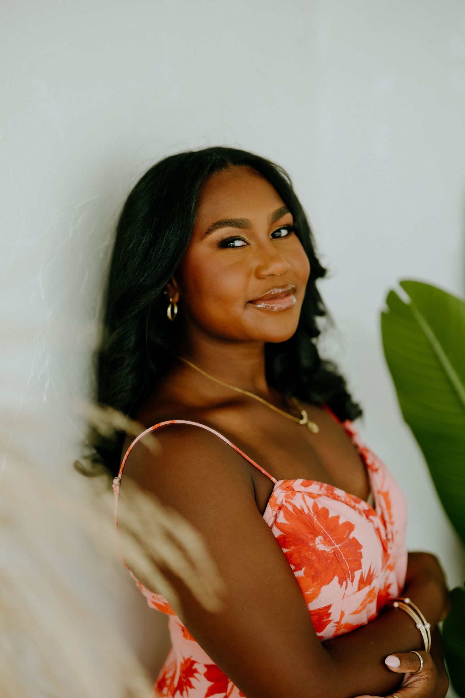 Portrait in coral floral dress with tropical plant decor.