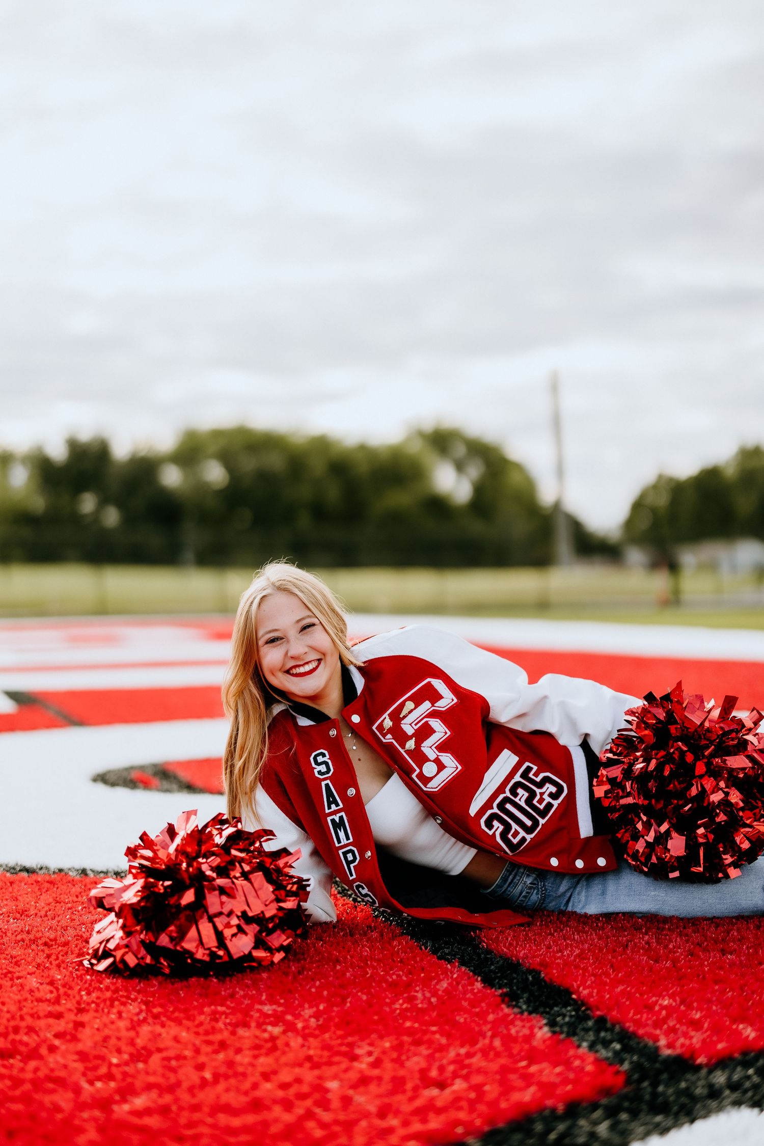 Cheerleader in red uniform lying on sports field with pom poms.