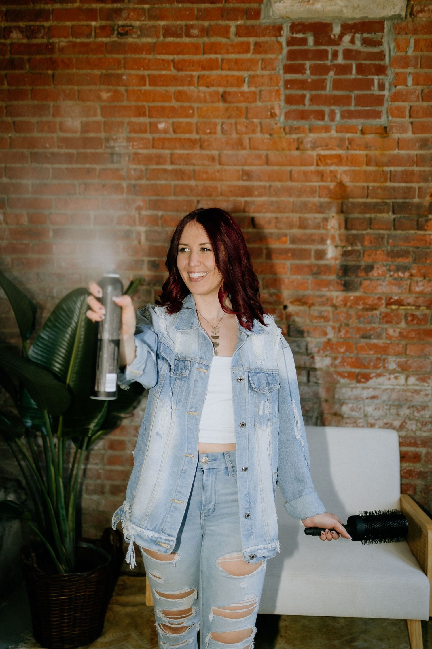 Casual denim outfit against exposed brick wall with indoor plant.
