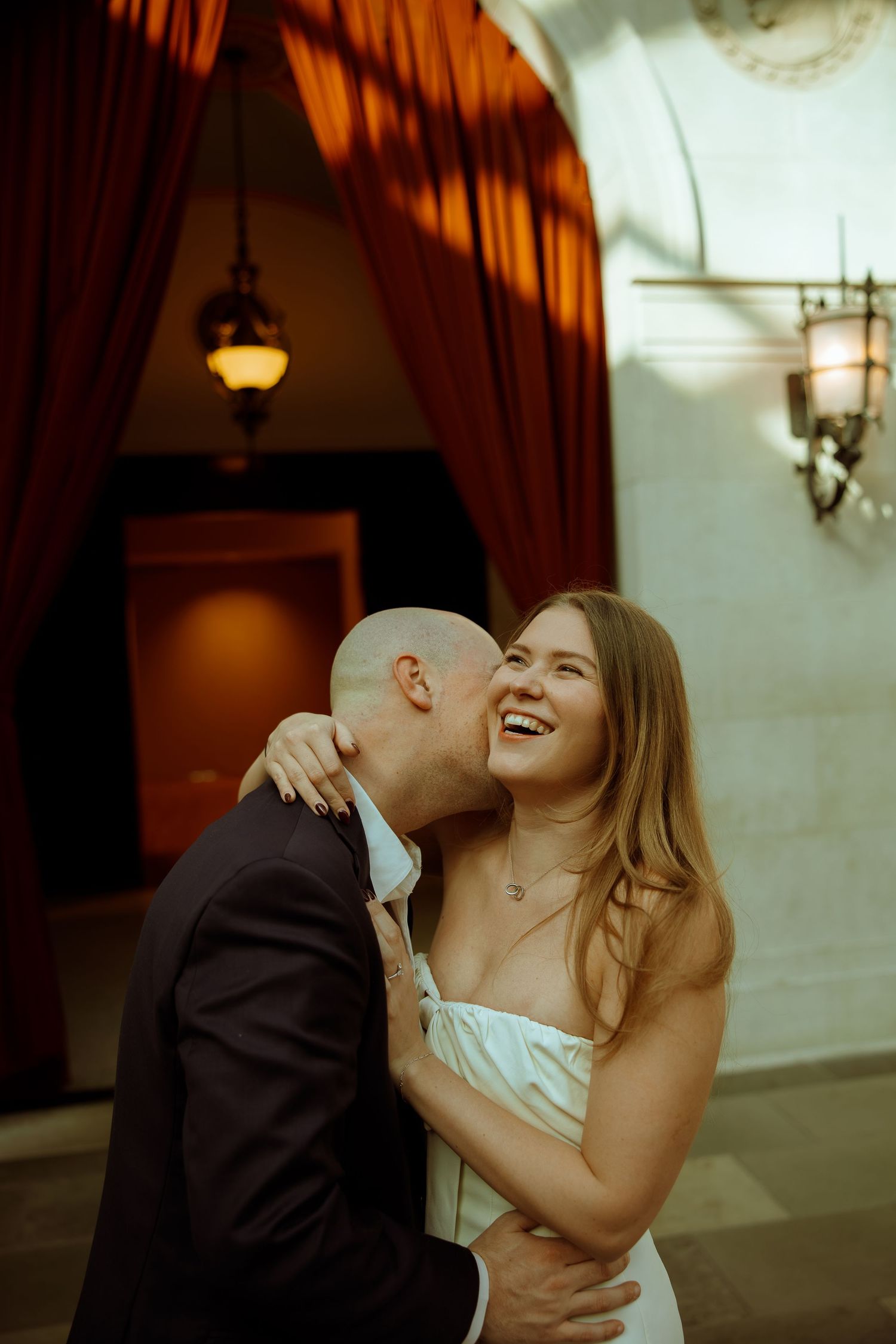 A couple shares an intimate moment laughing together in a warmly lit indoor venue with brick walls and hanging lamps.