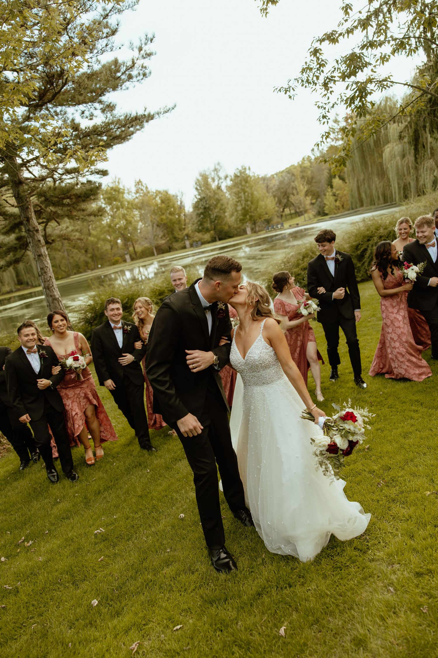 Wedding party celebrates outdoors on a grassy hillside with pine trees in the background.