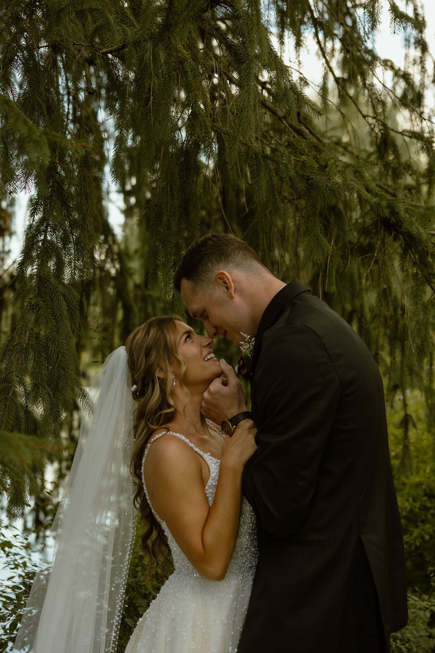 A romantic wedding moment captured under a weeping willow tree with soft natural lighting.