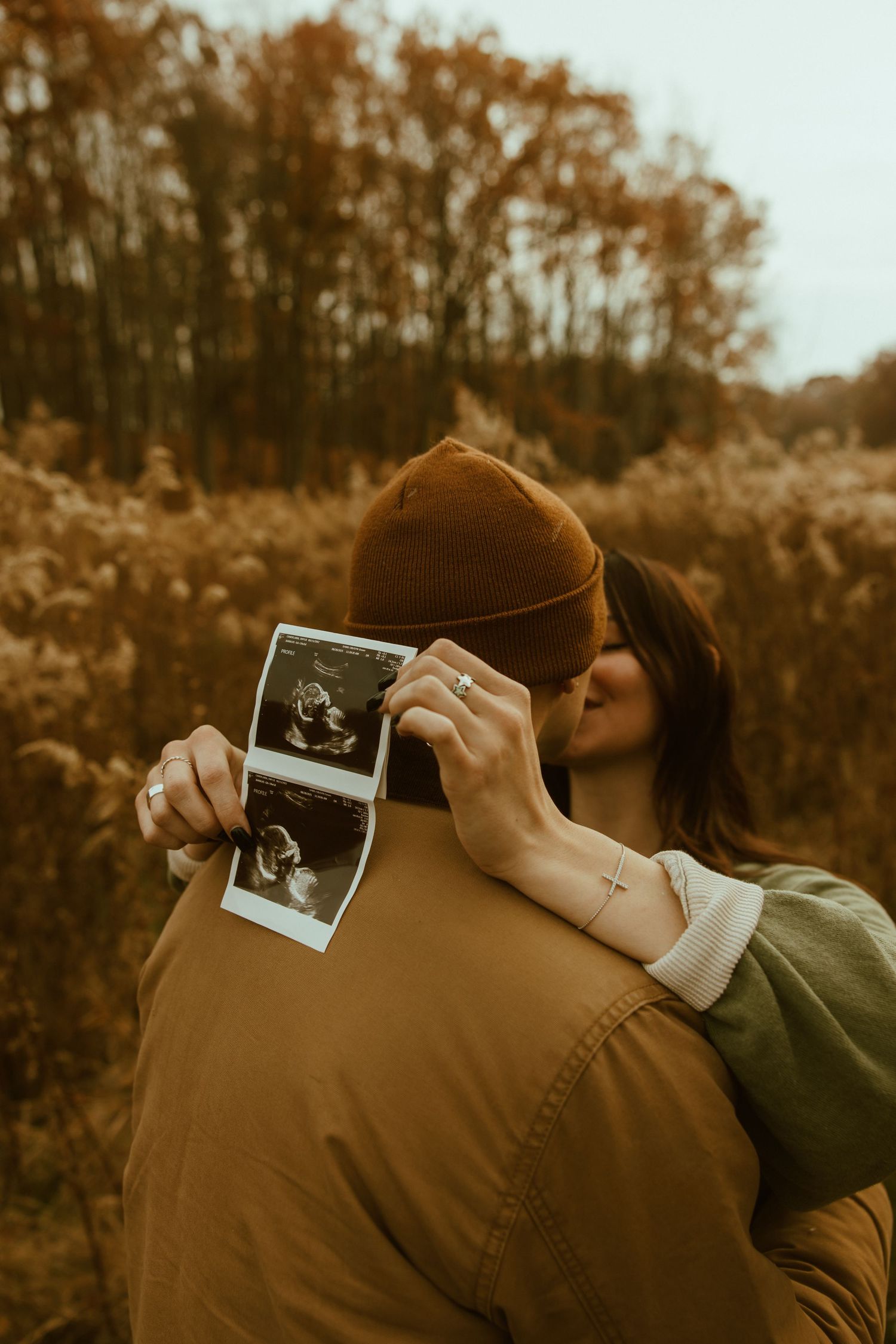 Close-up shots of hands holding ultrasound photos against an autumn forest background in warm sepia tones.
