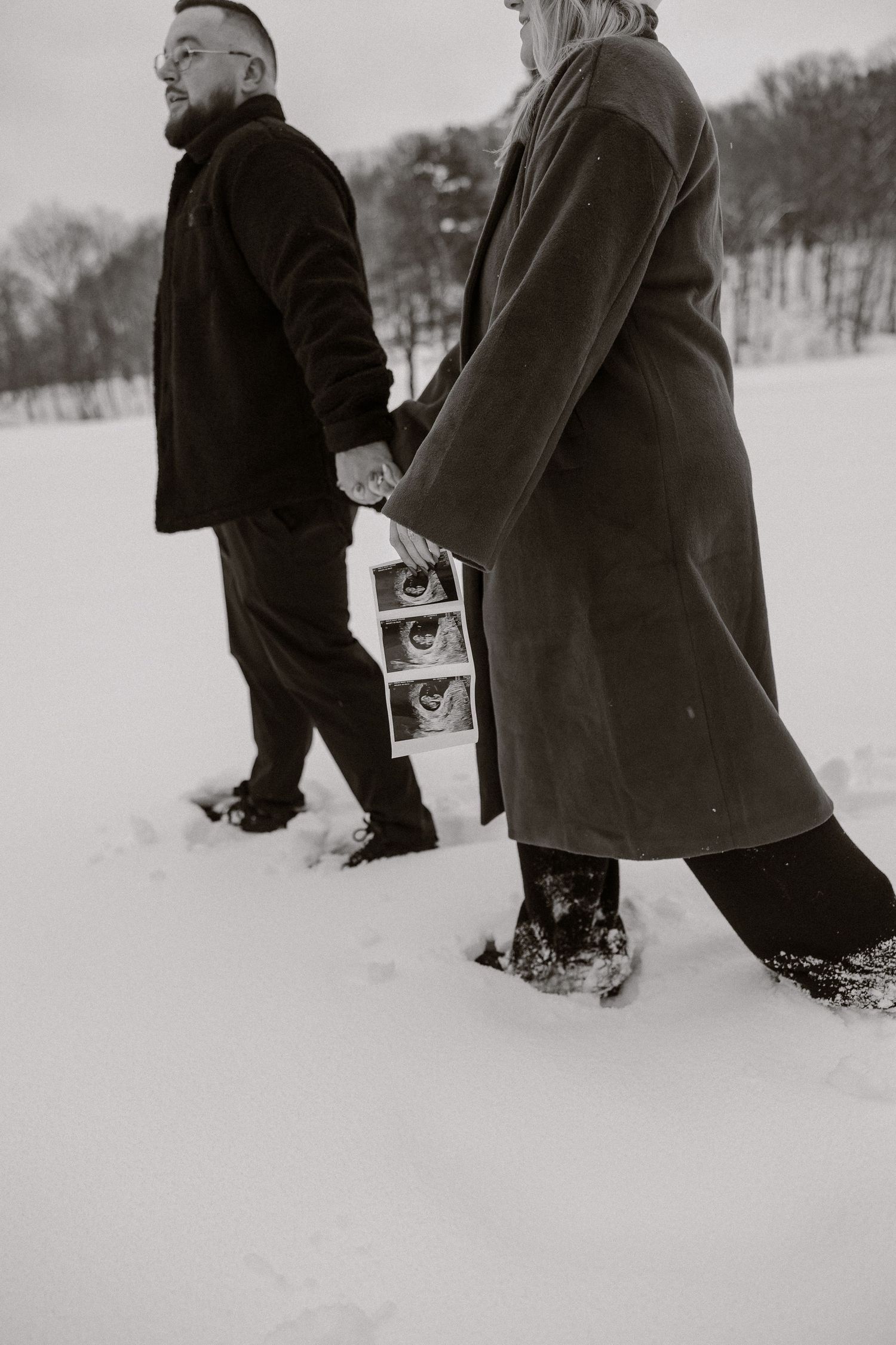 Two people walking through deep snow in winter while holding a photo or document between them.