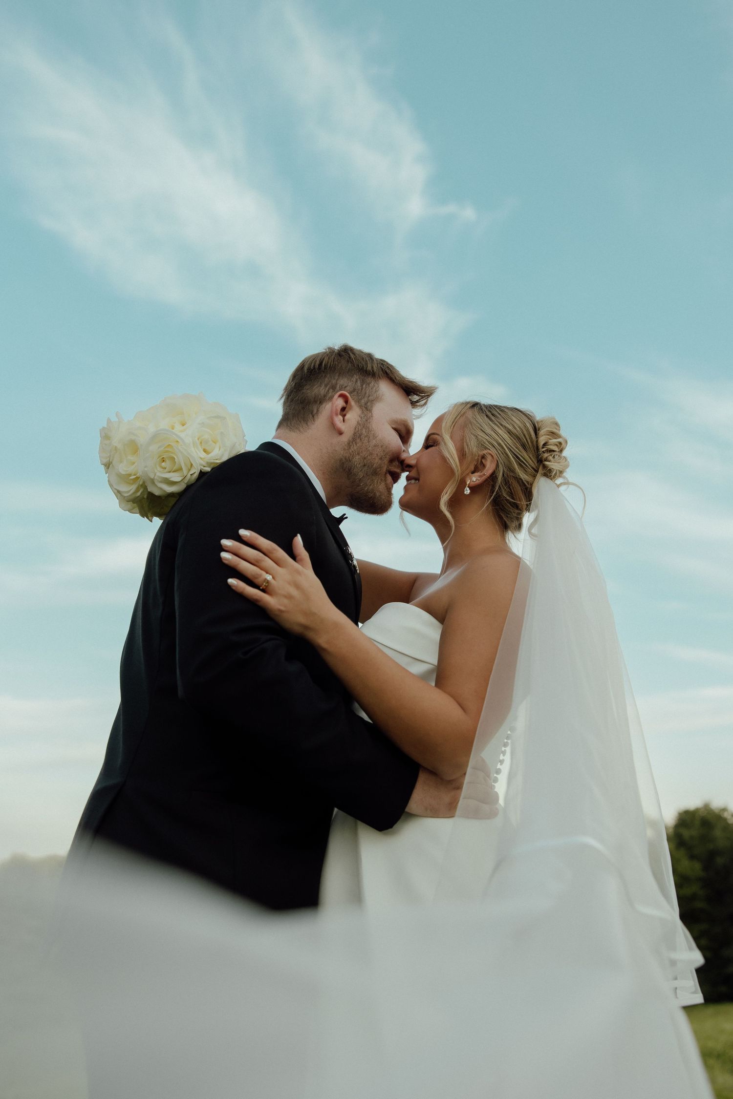 Romantic wedding couple sharing an intimate moment against a bright blue sky backdrop.