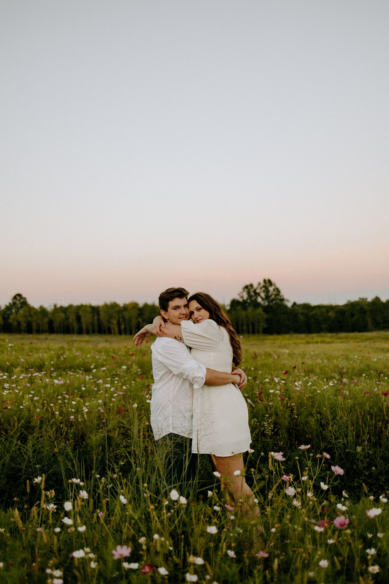 Loving couple embraces in a wildflower meadow during golden hour.