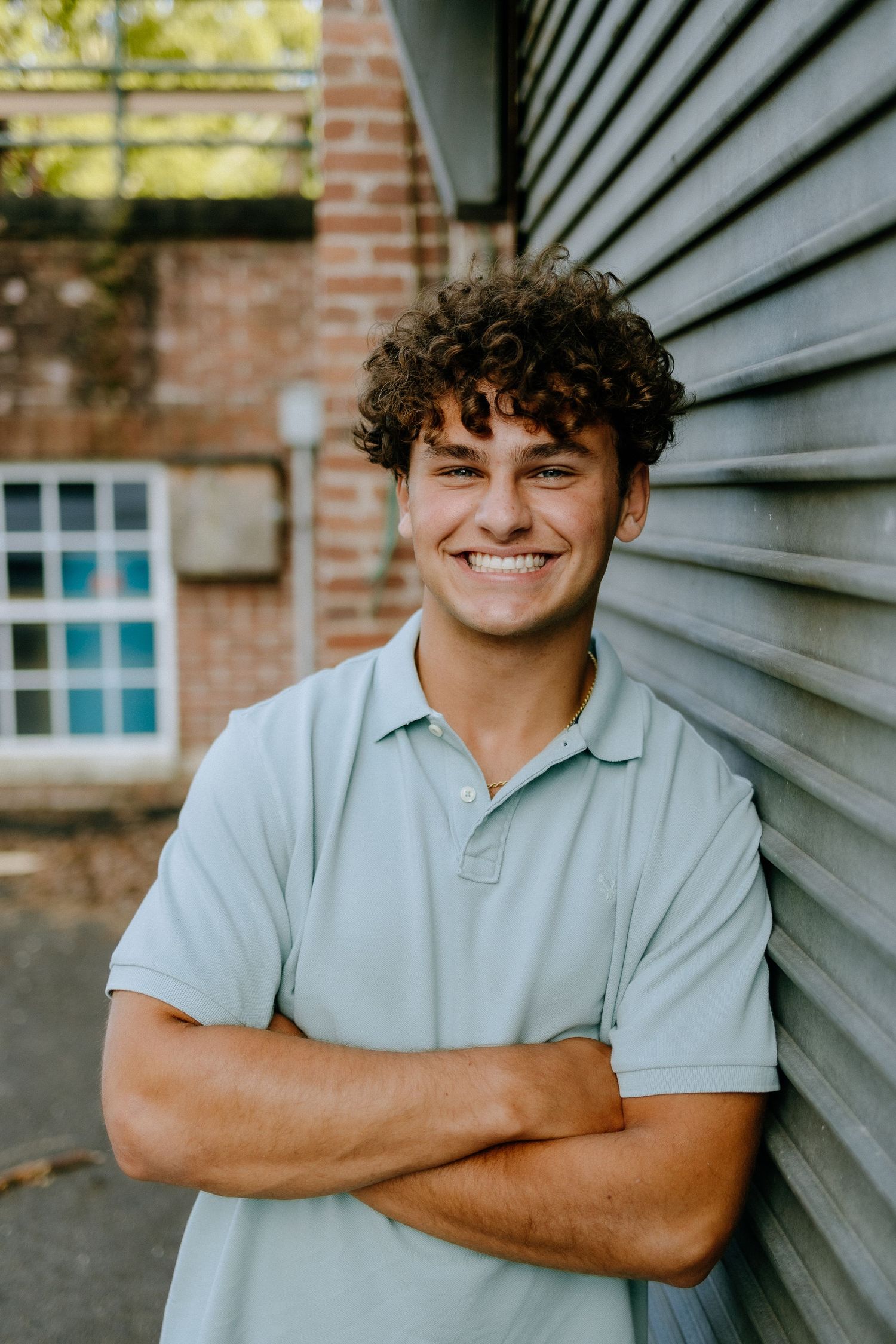 Casual outdoor portrait against gray siding and brick wall featuring a light blue polo shirt.