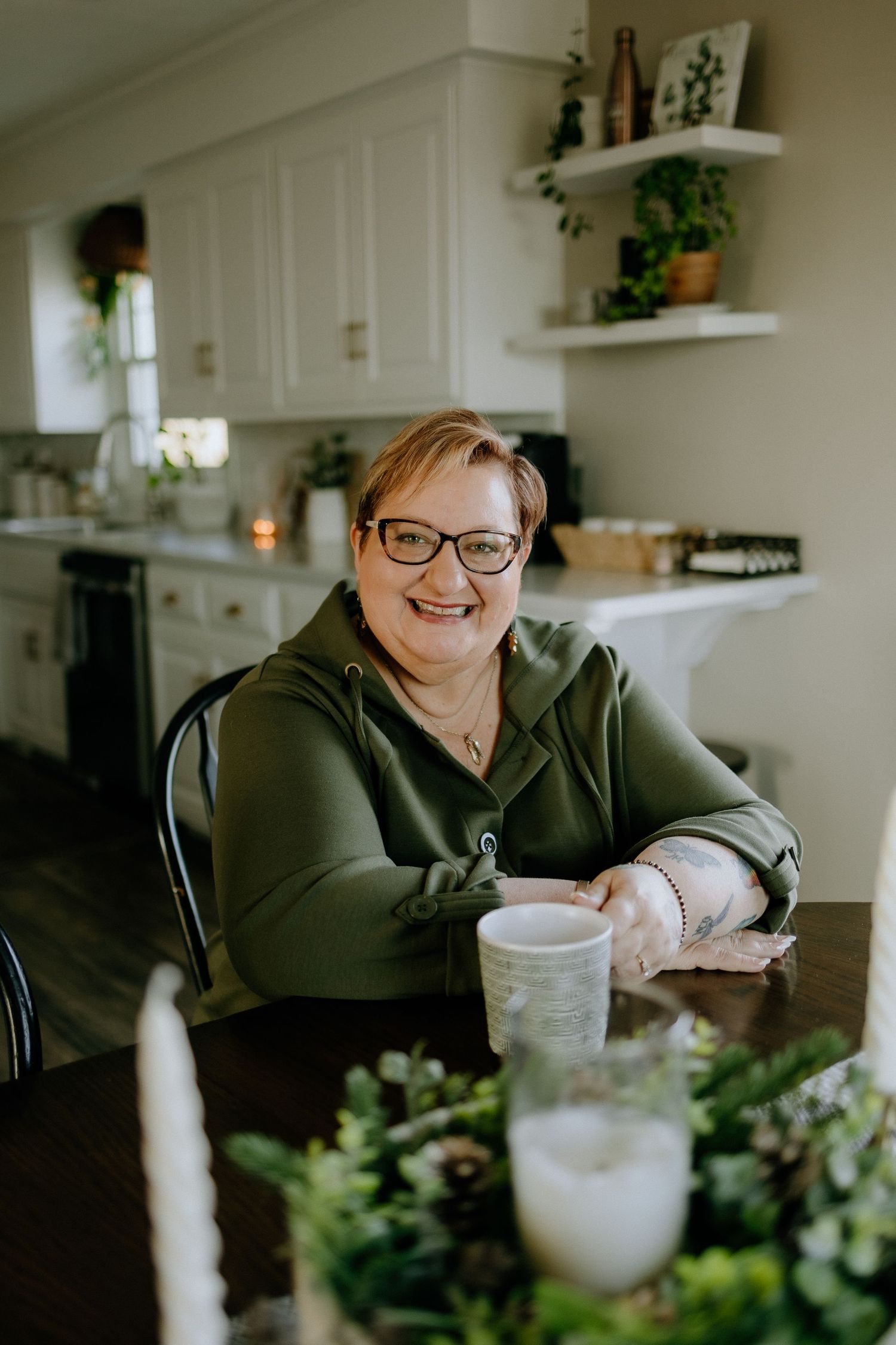 Person enjoying beverages at kitchen table with decorative plants and shelving in background.