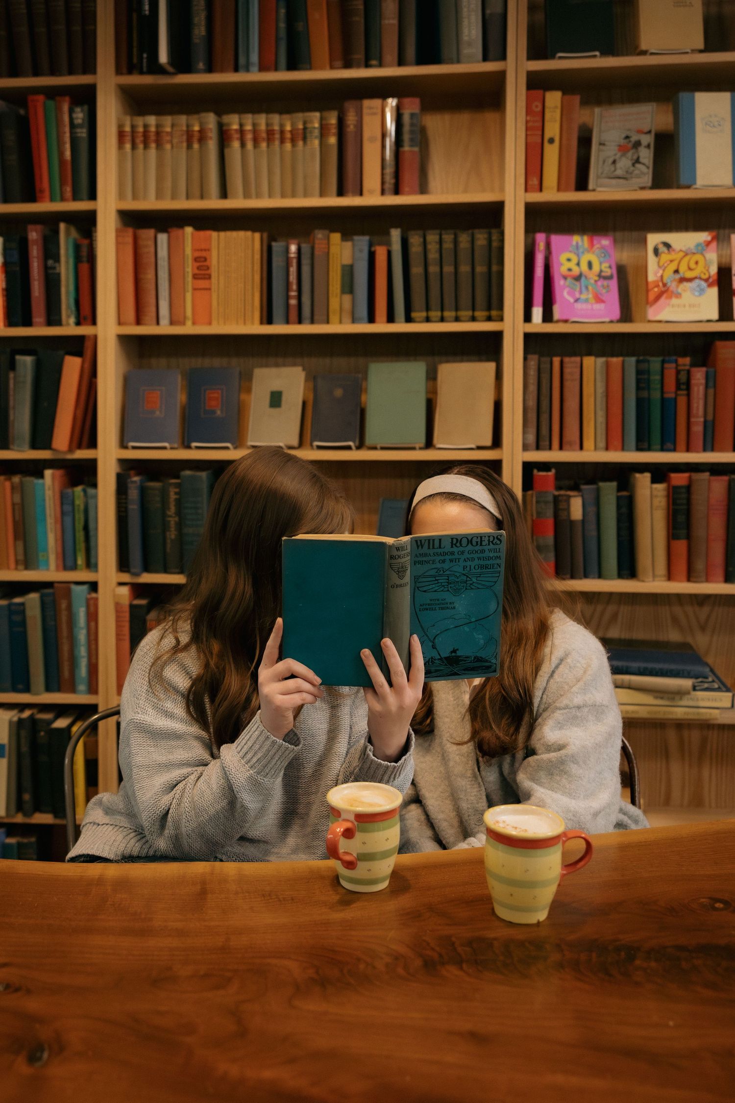 Two people sharing a book while drinking coffee in a cozy library setting.
