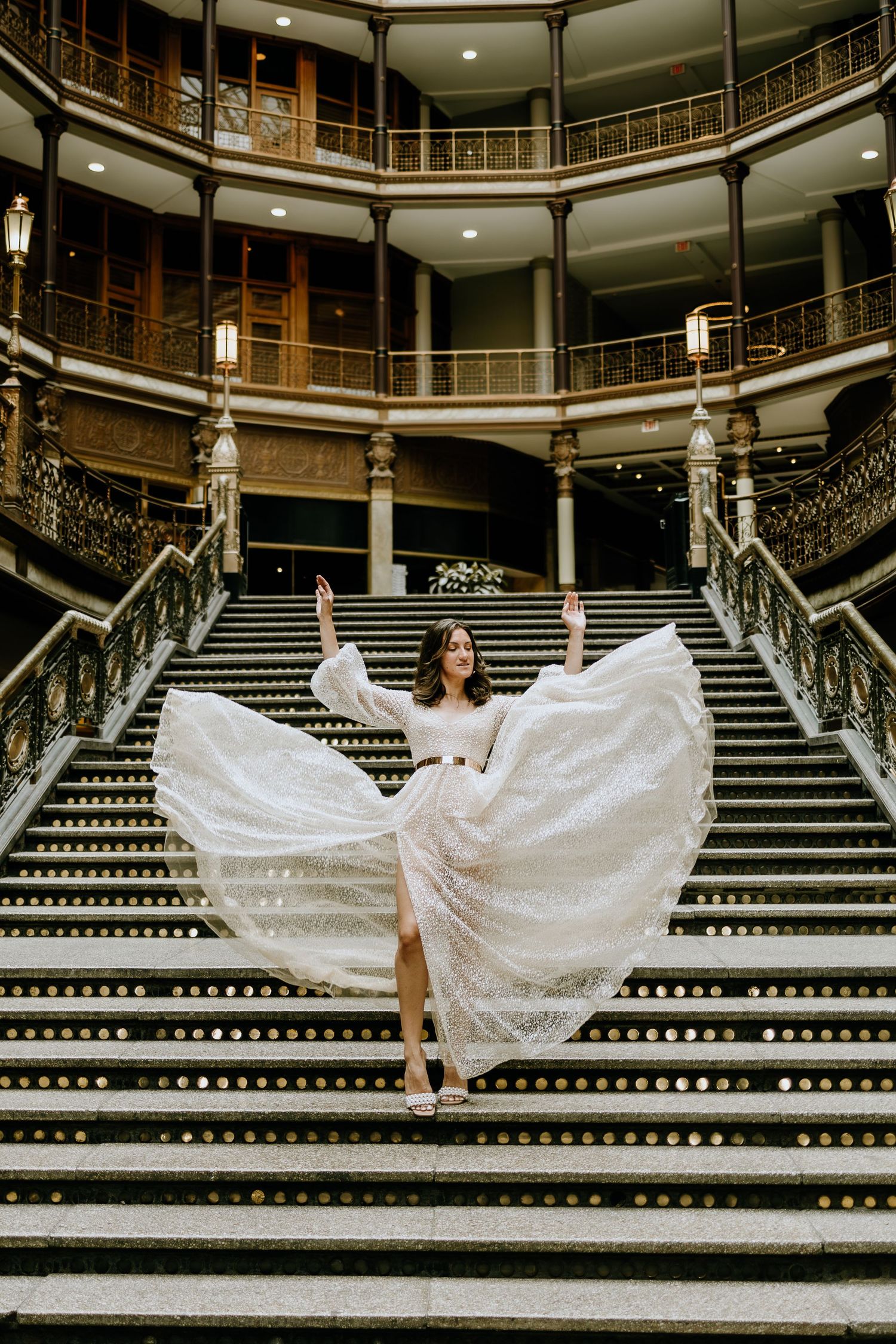 A dramatic white gown flourishes on ornate vintage stairs in a historic building.