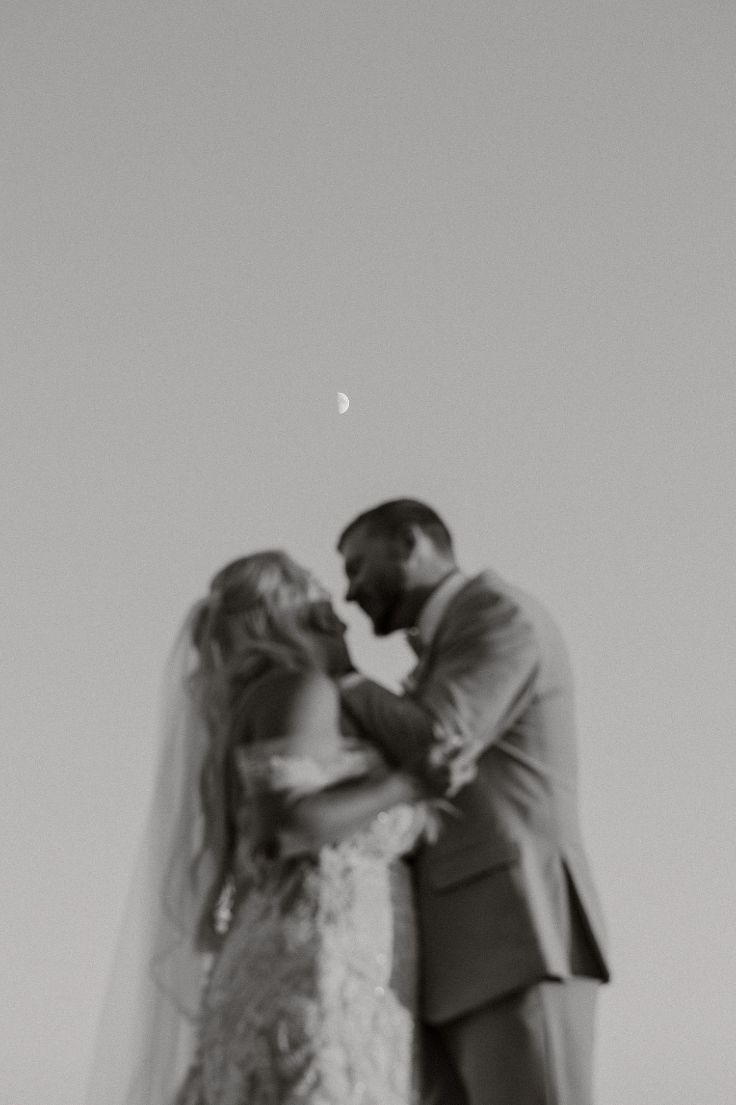 A black and white wedding portrait captures a tender kiss between newlyweds.