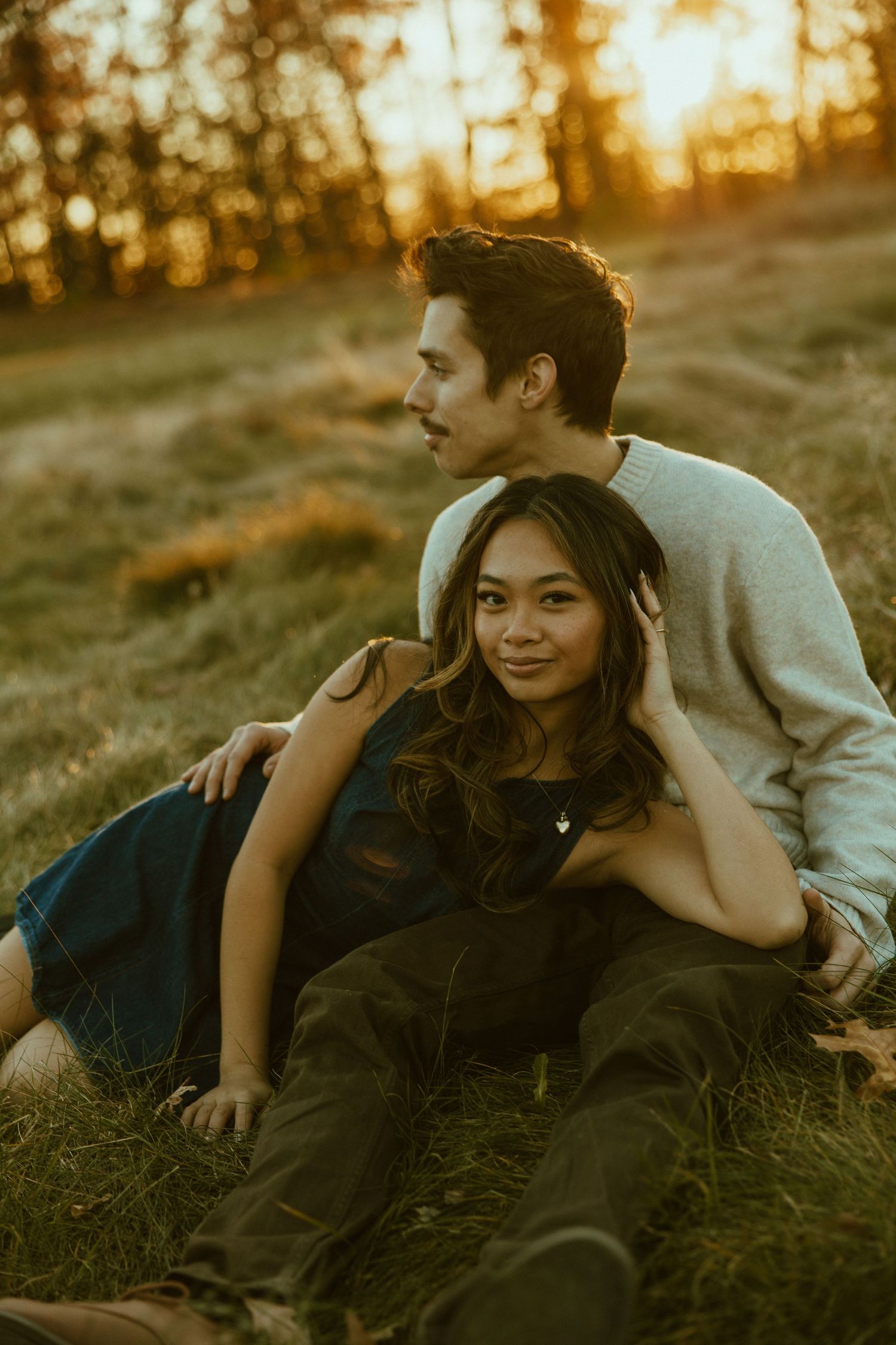 A couple sharing intimate moments while laying in grass during golden hour sunset.