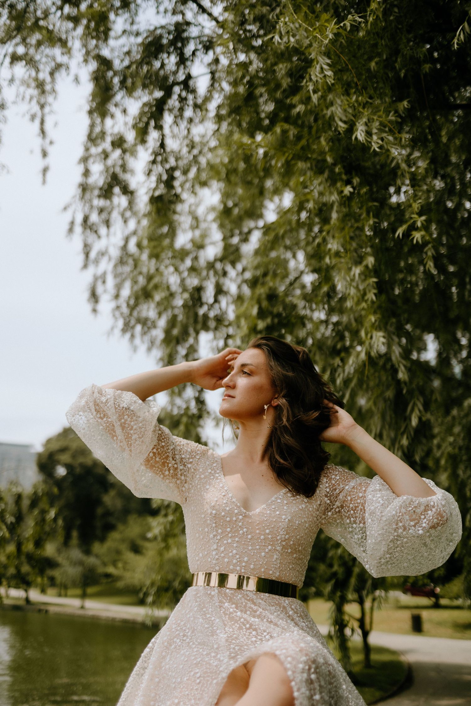 A sparkly white dress twirls gracefully by a peaceful pond on a sunny day.