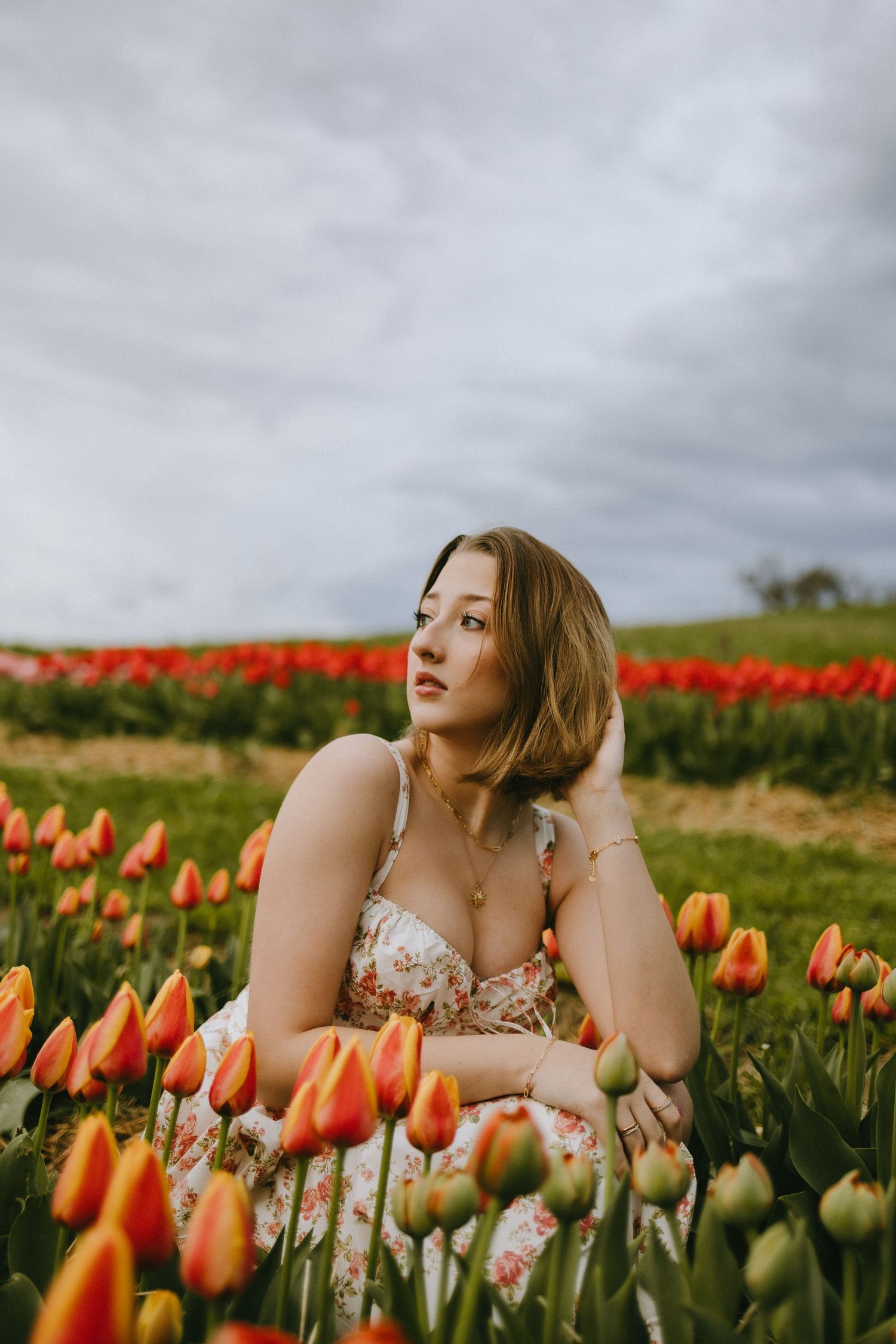 A dreamy portrait among vibrant orange and red tulips under moody skies.