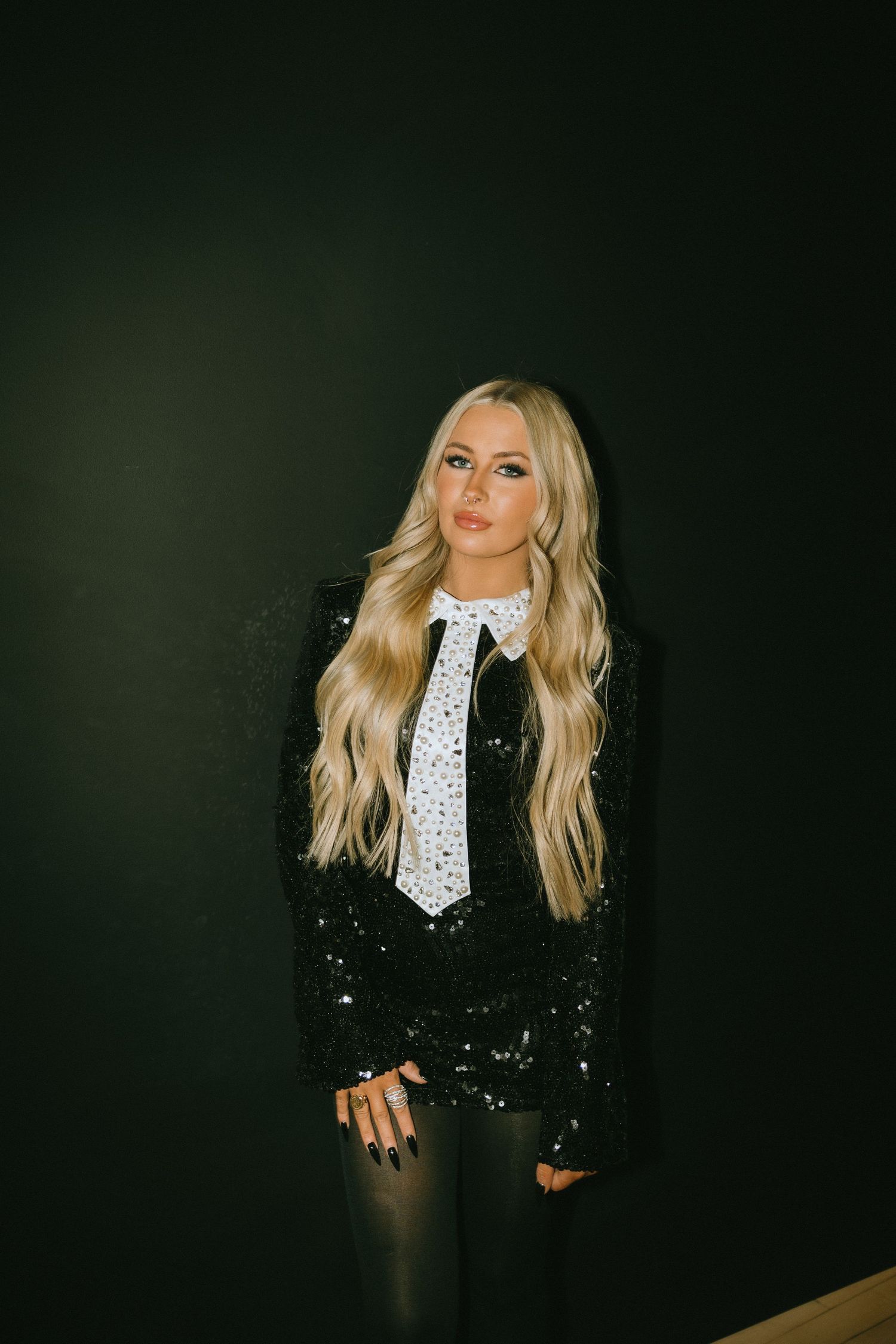 Glamorous portrait in black sequined jacket with white embellished tie and long blonde hair.