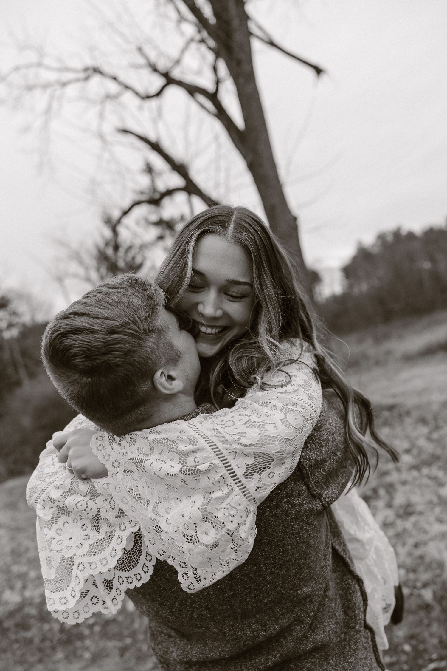 A romantic black and white photo of a couple embracing and laughing together outdoors on a winter day.