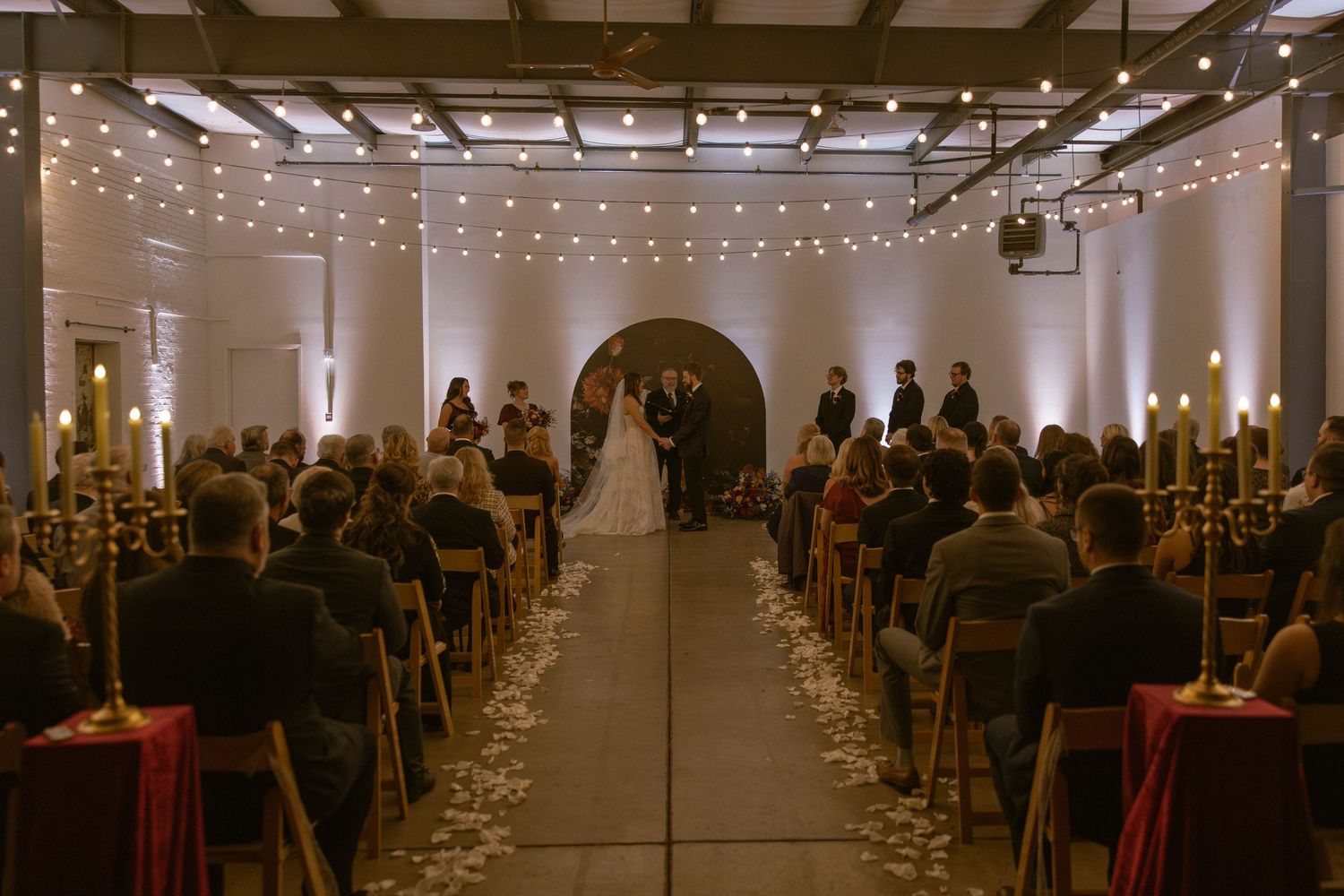 Elegant indoor wedding ceremony space with string lights and rows of chairs filled with guests.