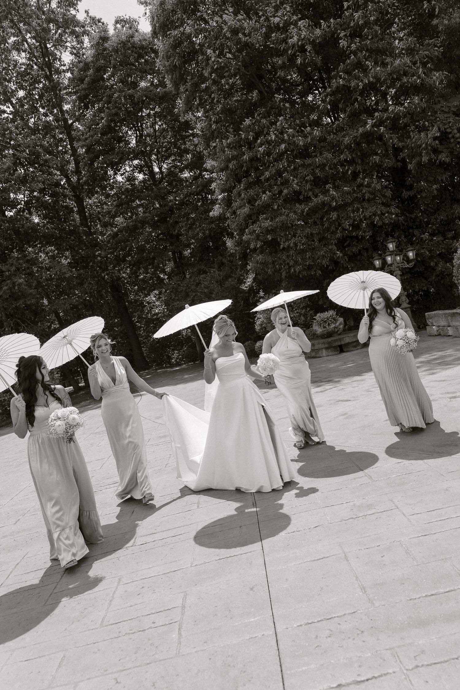 A group in white dresses and parasols performs a choreographed dance routine on an outdoor stage in black and white.