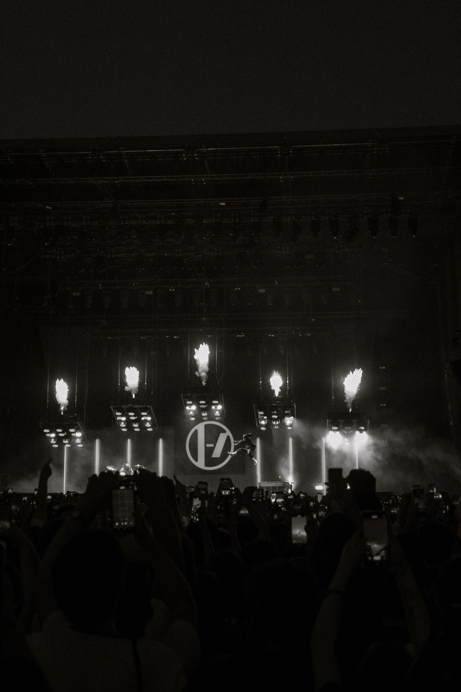 Concert venue with bright stage lights illuminating band logo and crowd silhouettes in black and white.