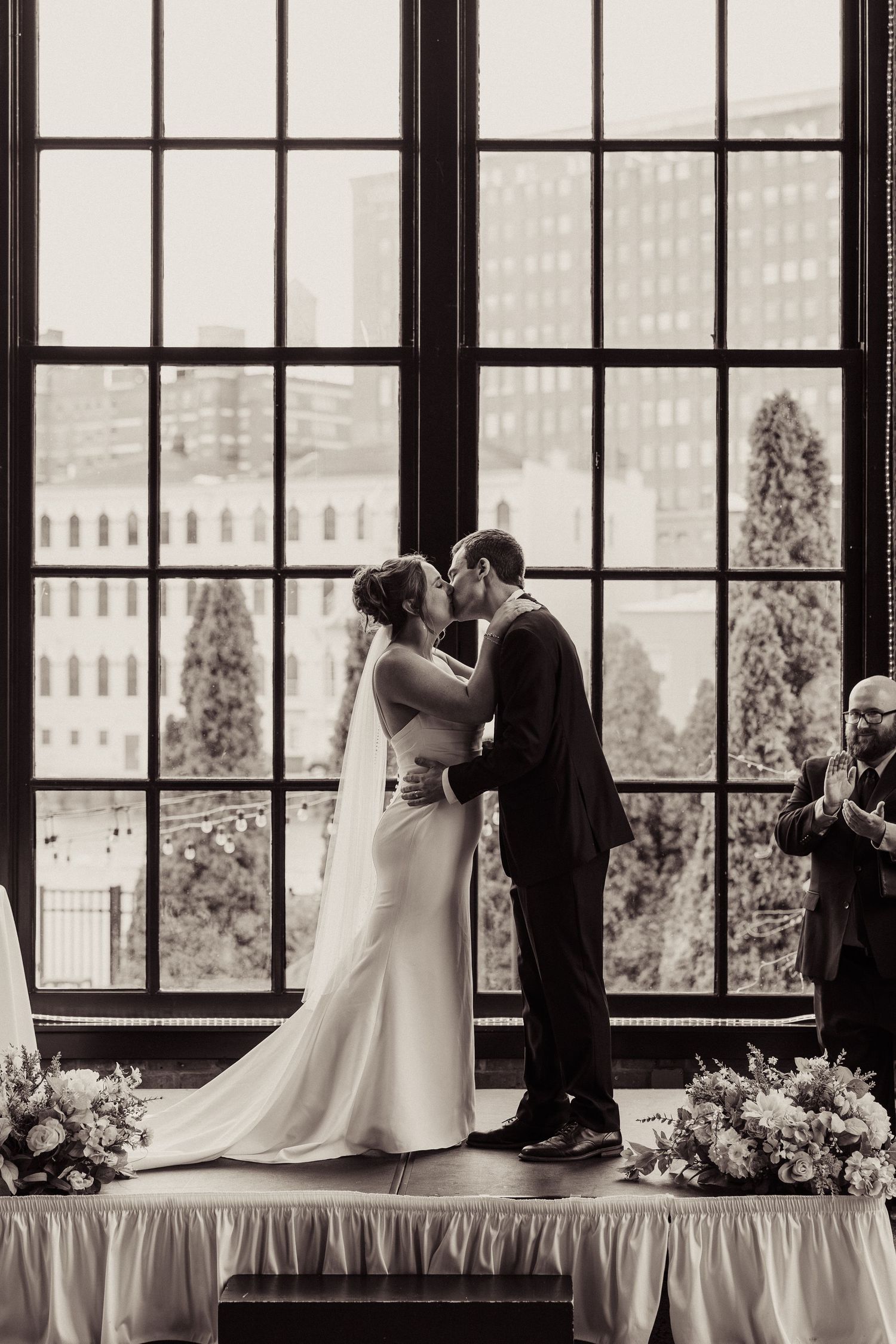 Black and white wedding ceremony photos in front of large industrial windows with city views.