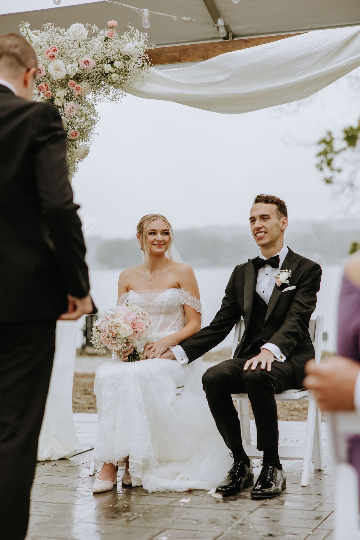 Newlyweds participate in a playful foot washing ceremony during their wedding under a white canopy.