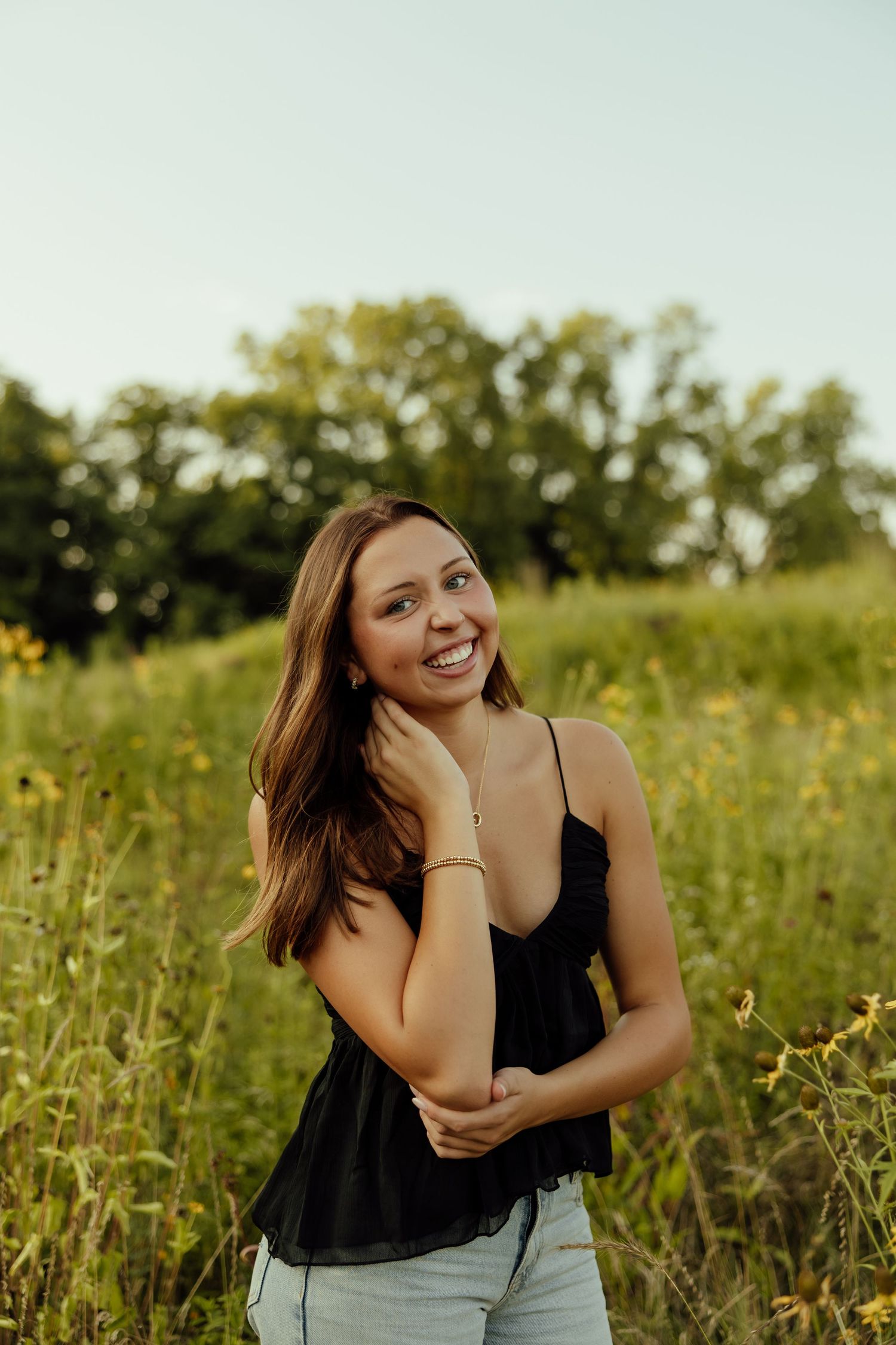 A series of candid outdoor portraits showing a person in a black tank top and jeans posing in a sunny wildflower field.