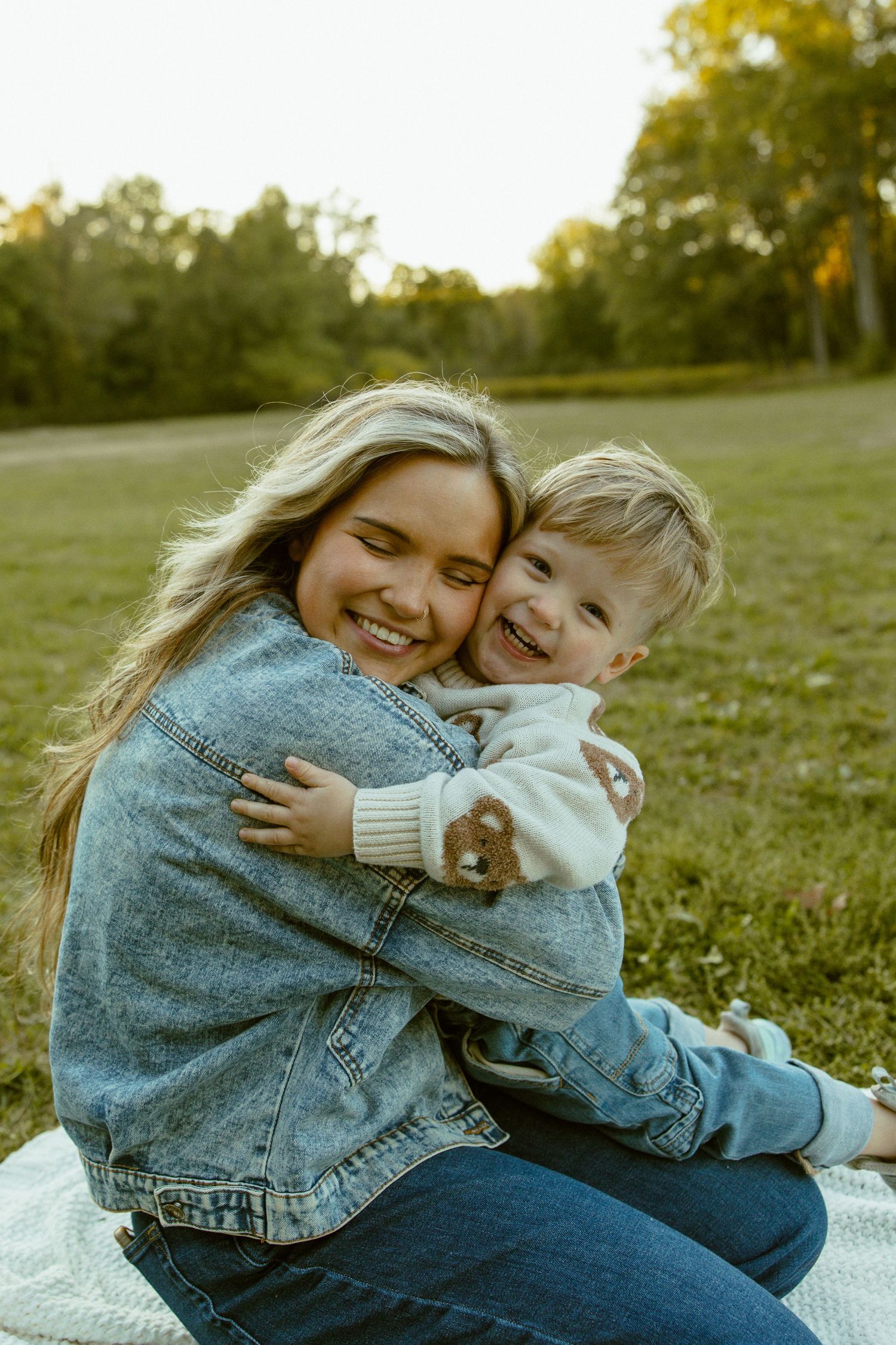 Two people share joyful laughter while relaxing on a blanket in a sunny grassy field.