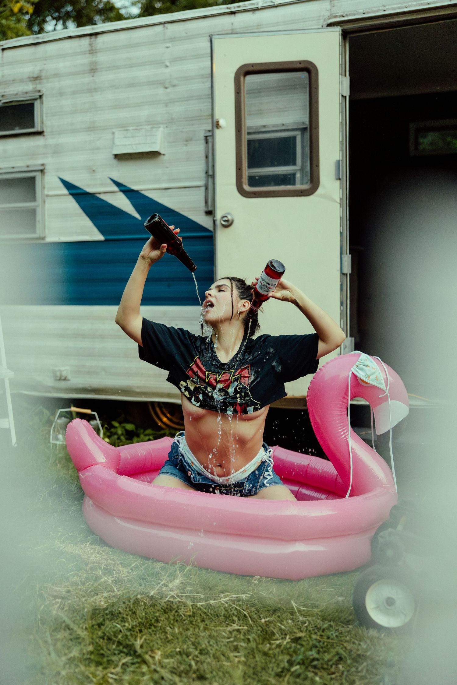 Someone relaxing in a pink inflatable pool while drinking from a bottle near a white trailer.