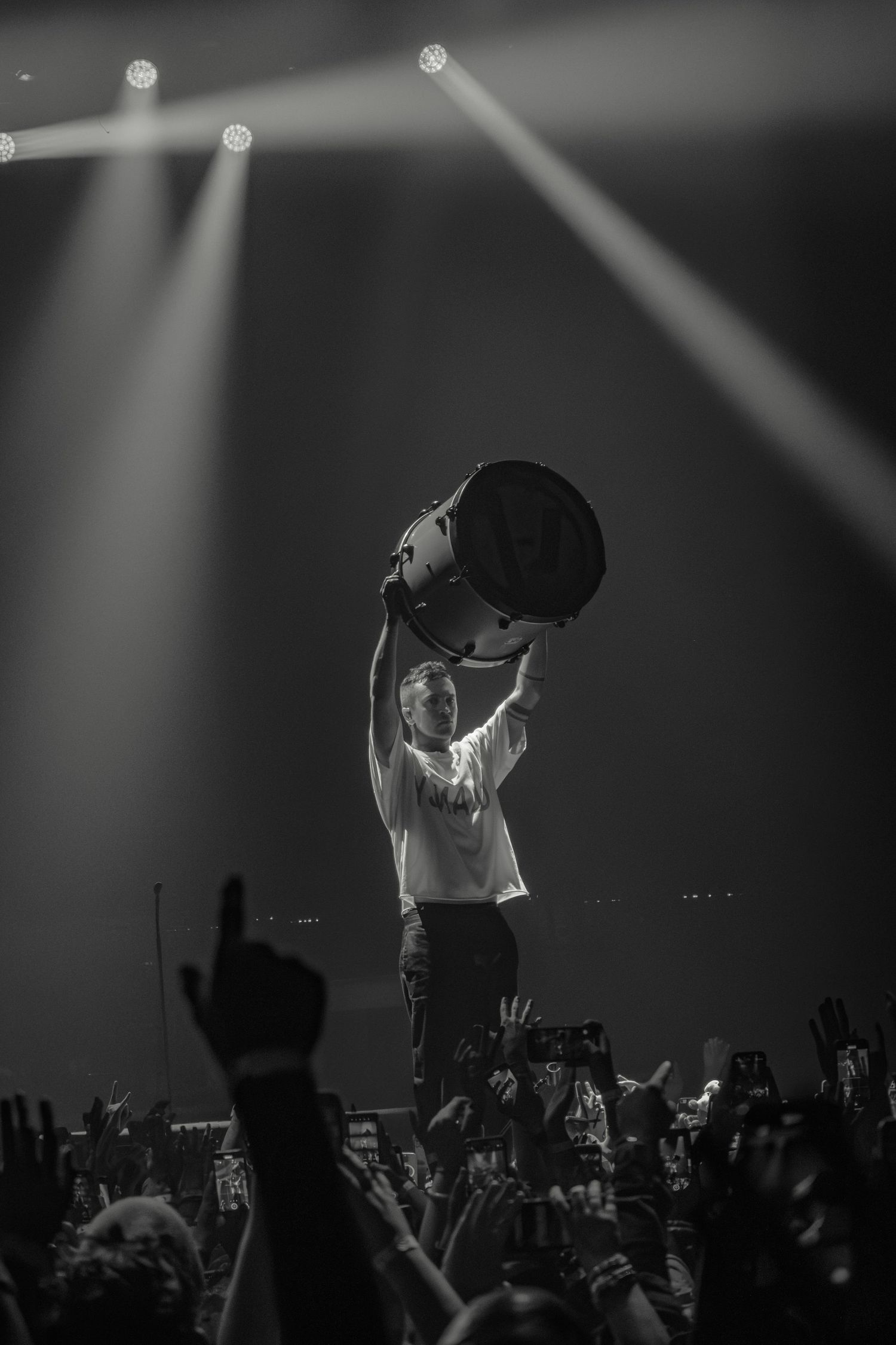 Concert performer stands dramatically backlit on stage as crowd raises hands.
