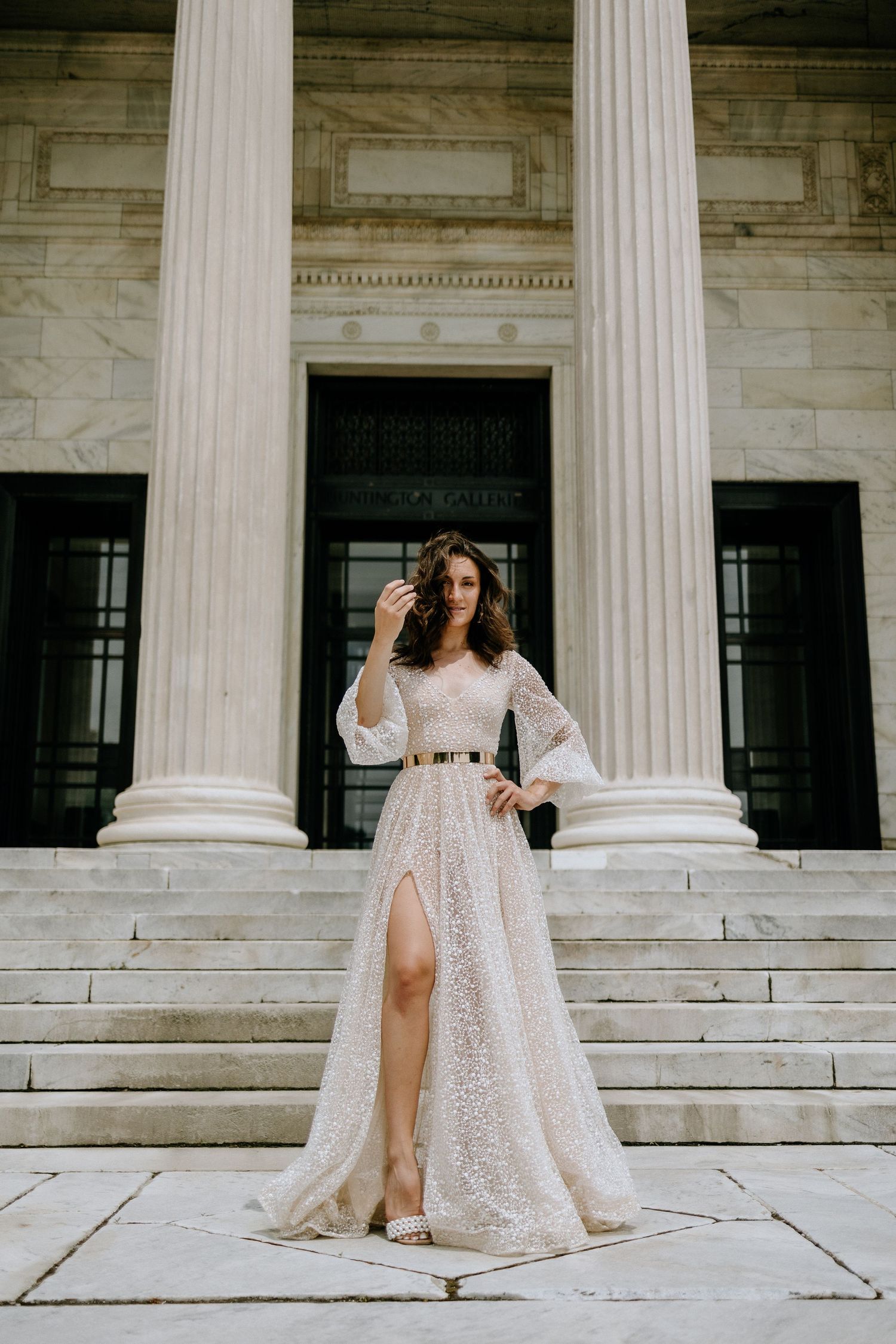 Elegant white lace dress with bell sleeves photographed against classic marble columns and steps.